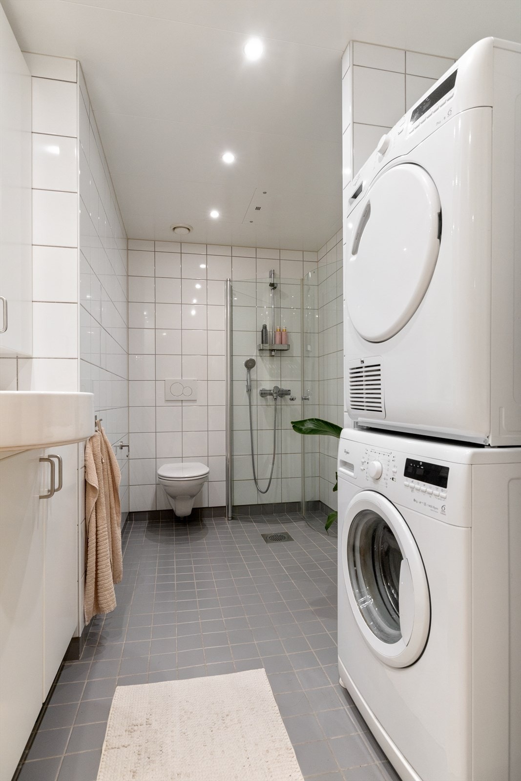 Badet er utstyrt med vegghengt toalett, dusjhjørne med innfellbare glassdører og opplegg til både vaskemaskin og tørketrommel. Galleribilde