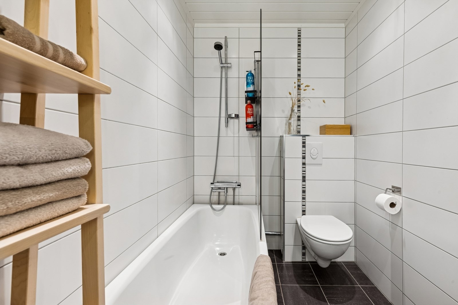 Badet har vegghengt toalett, heldekkende servant i innredning og badekar med veggdusj og glassvegg. Galleribilde