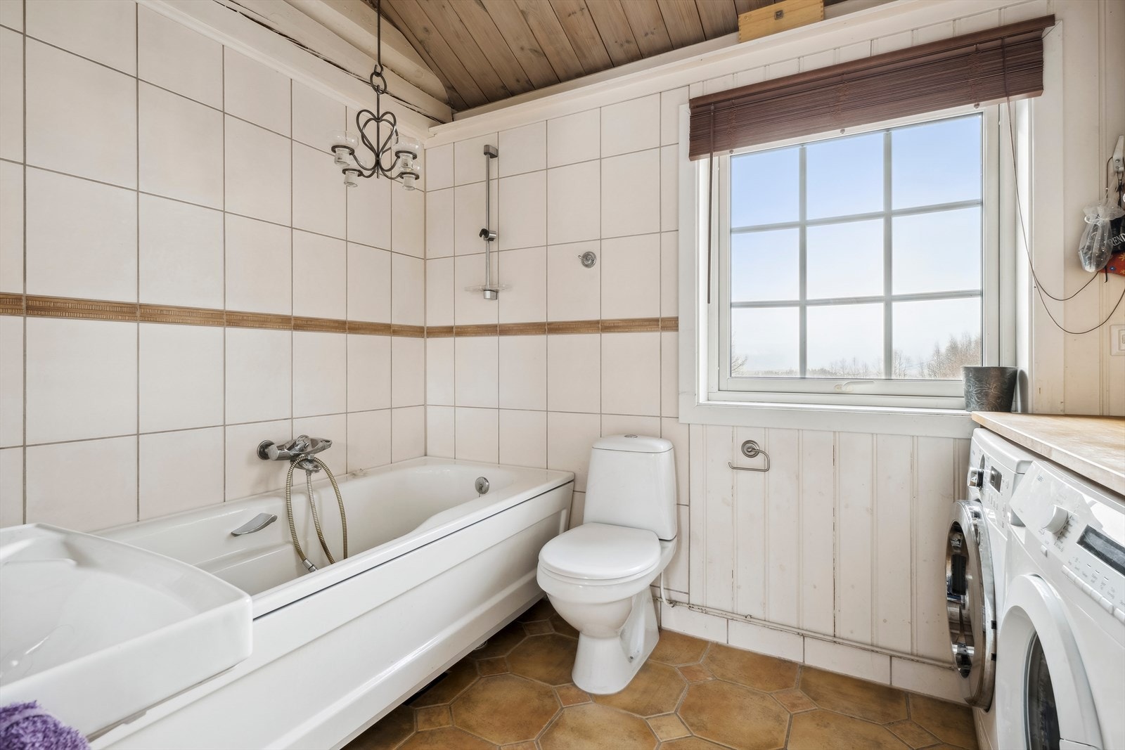 Kombinert bad og vaskerom med toalett, badekar, servant og opplegg for vaskemaskin. Galleribilde