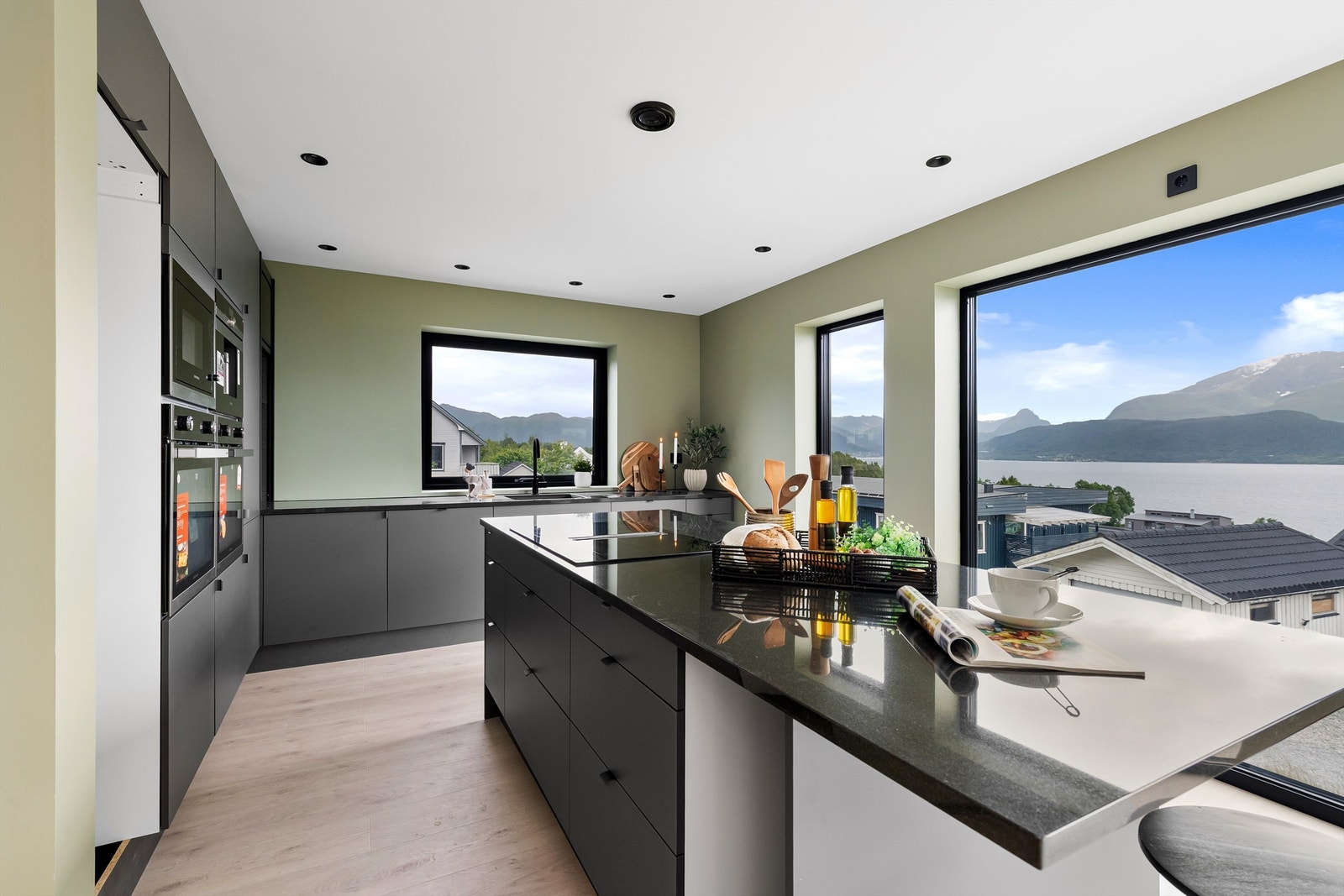 Kjøkkenøy med nedfelt induksjonstopp med innebygd ventilator. Benkeplate i stein og det er sitteplasser på enden på spiseøyen Galleribilde