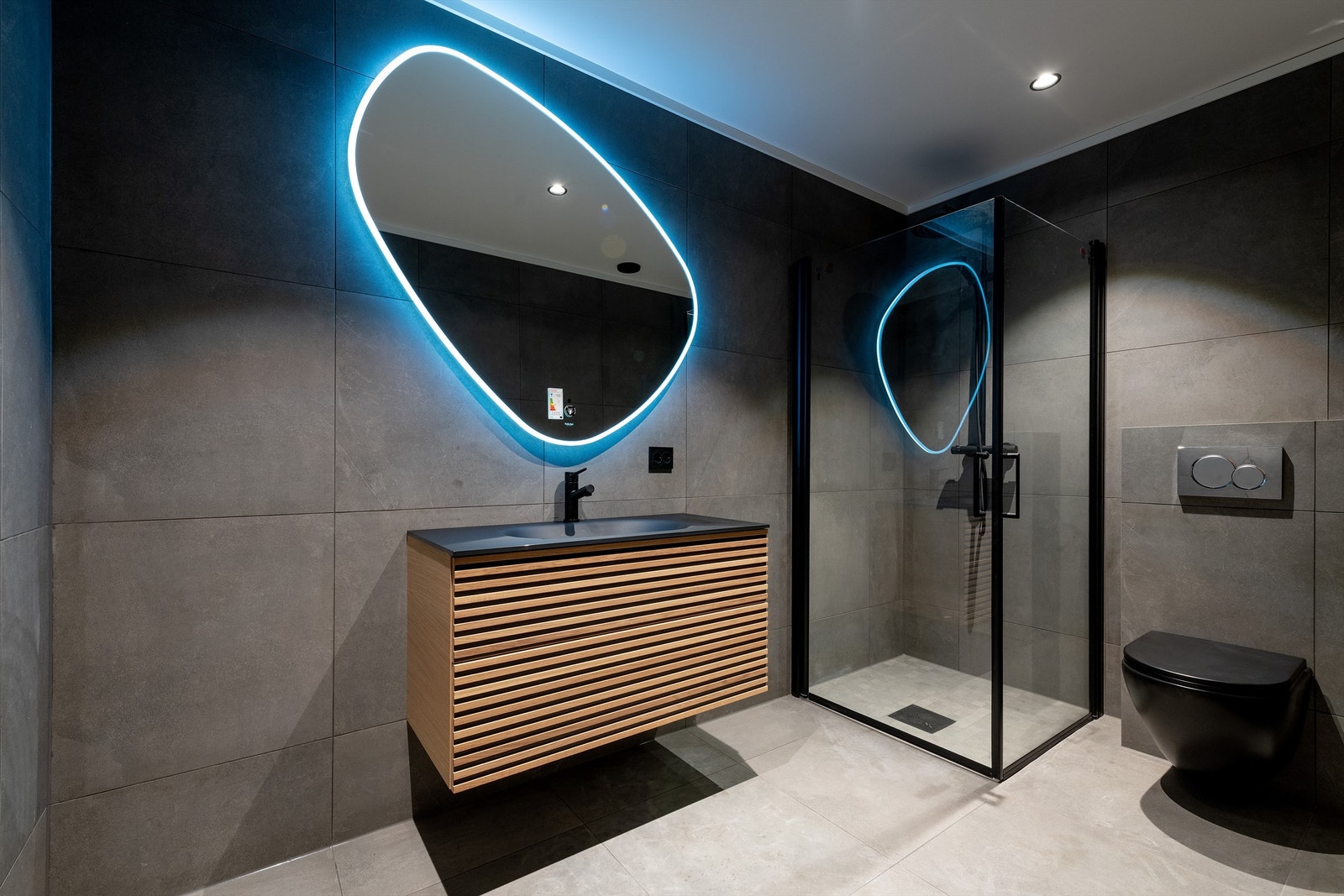 Flislagt bad i underetasjen. Innredning med ovenpåliggende armatur, speil med lys, dusjhjørne med glassvegger og vegghengt dusjarmatur med hånddusj og regndusj. Vegghengt toalett Galleribilde