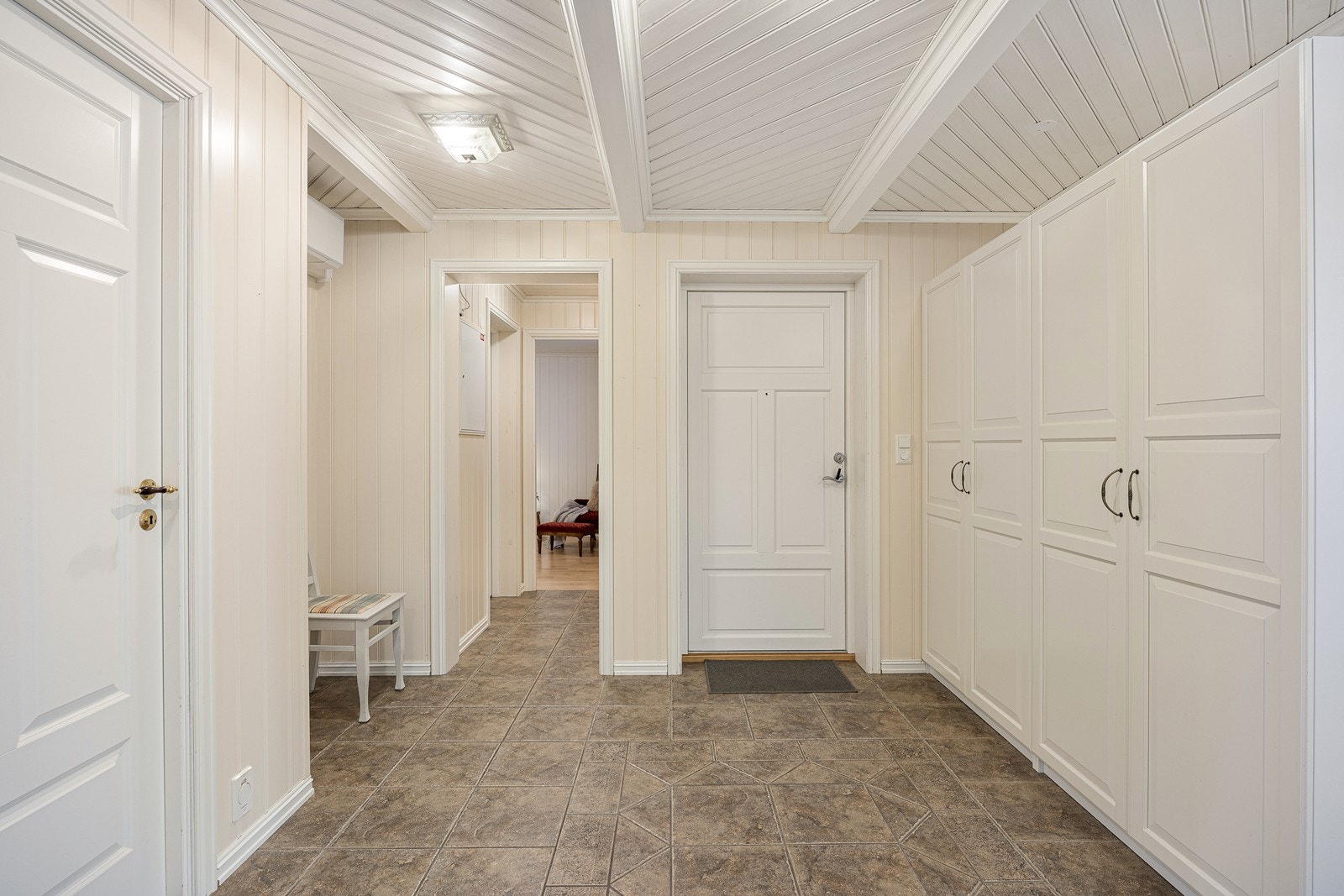 Vel inne har entreen hvite takbjelker, lysmalte panelplater og grå gulvfliser med varme. Yttertøyet ryddes enkelt bort i et dobbelt garderobeskap med hvite, profilerte fronter. Galleribilde