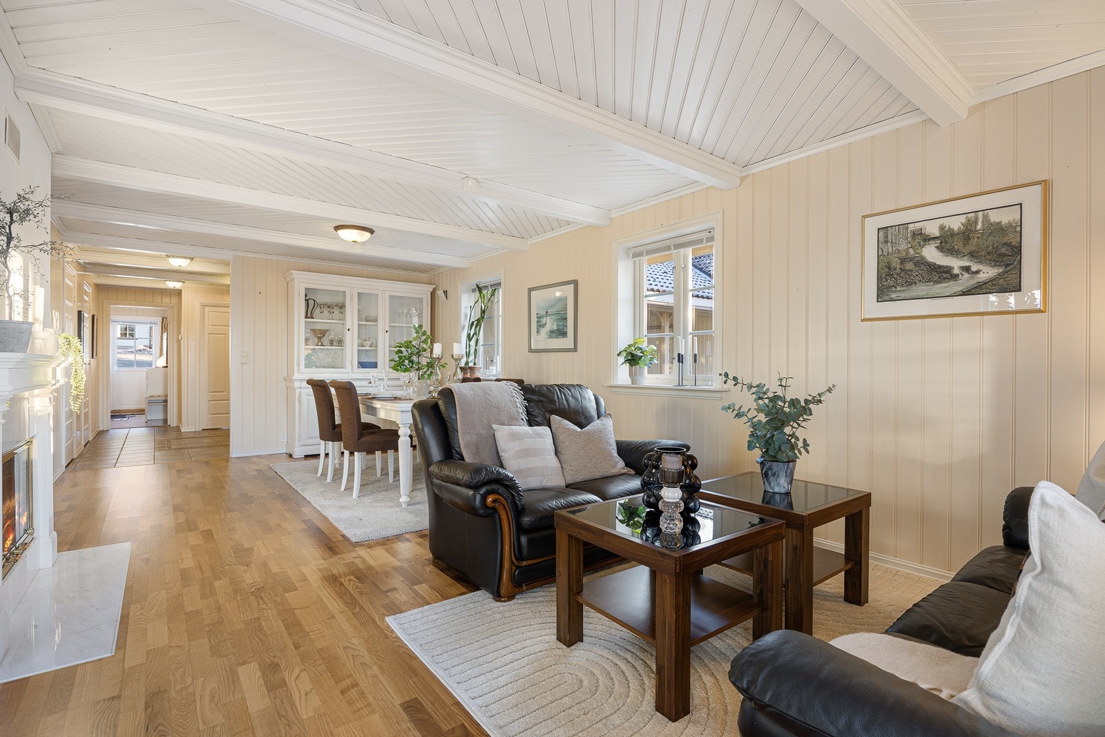 Parkett med varme på gulvet kombineres med lyse panelplater, og stuen har samme type tak som entreen - paneler med synlige bjelker malt i hvitt. Galleribilde