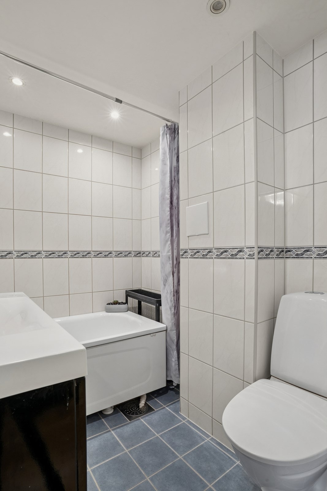 Badet er innredet med servantskap med ett-greps blandebatteri, gulvstående toalett, dusjgarnityr og badekar, samt opplegg for vaskemaskin. Galleribilde