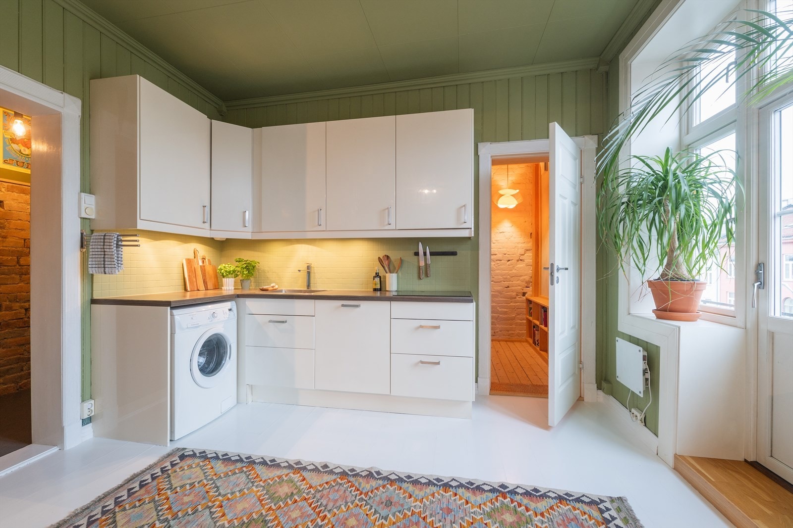 Kjøkkeninnredningen har et stilrent design med hvite, glatte fronter, malte fliser på vegg over kjøkkenbenken og benkeplate i laminat. Galleribilde