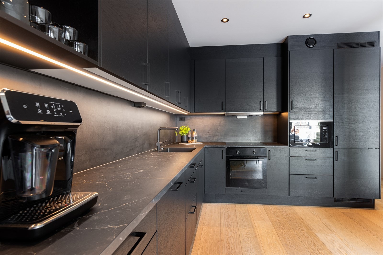 Kjøkkeninnredningen fra Sigdal i mørk utførelse har godt med oppbevaringsplass, med takhøye overskap, seksjon med høyskap og åpne hyller. Det er gode arbeidsflater på laminerte benkeplater med nedfelt induksjonstopp og oppvaskkum. Galleribilde