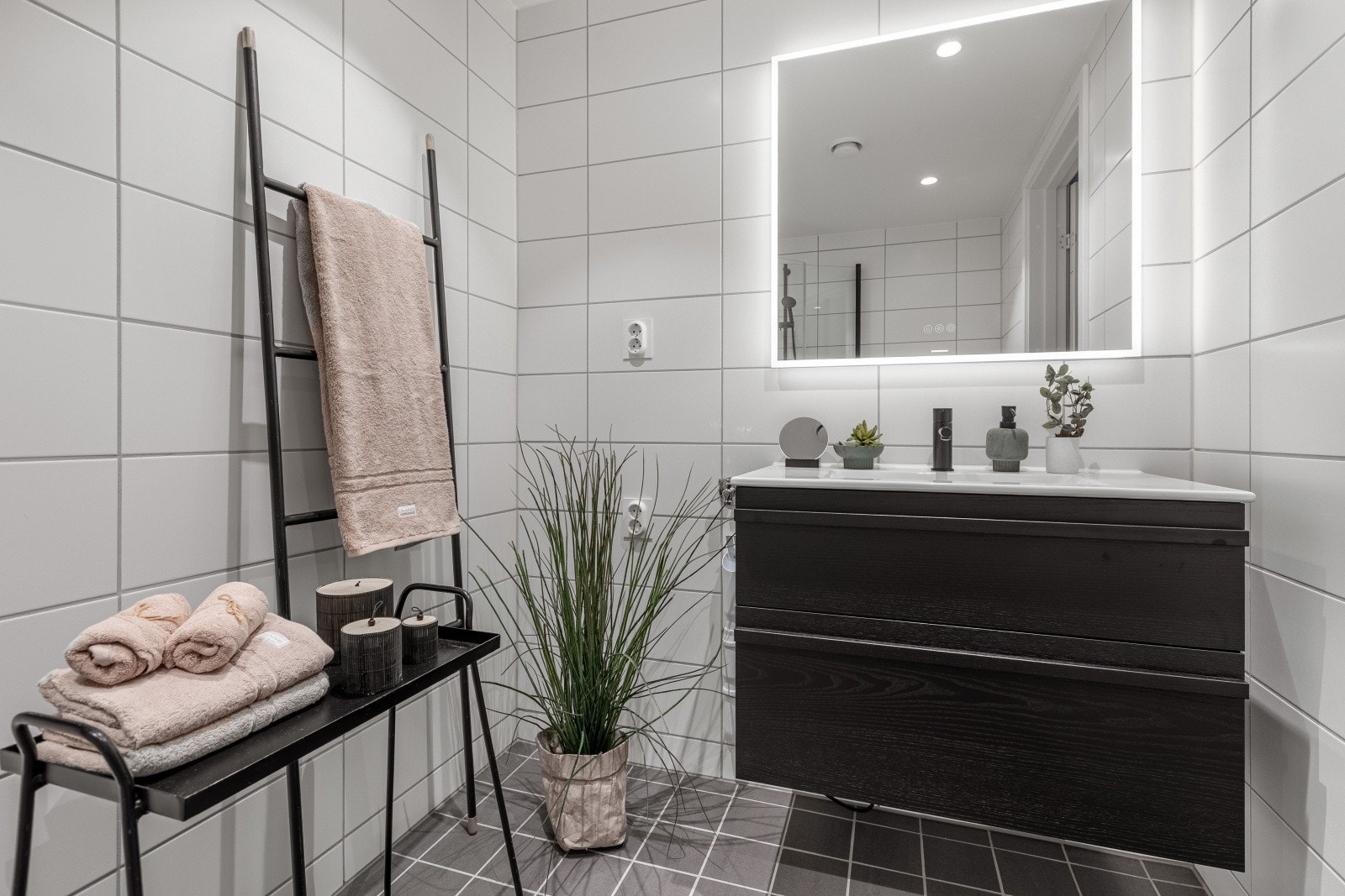 Baderommet har en tidløs baderomsinnredning med skuffeseksjon, speil med tilhørende lys, vegghengt toalett og dusjnisje med innfellbare glassdører. I tillegg er det opplegg for vaskemaskin og tørketrommel i søyle. Galleribilde