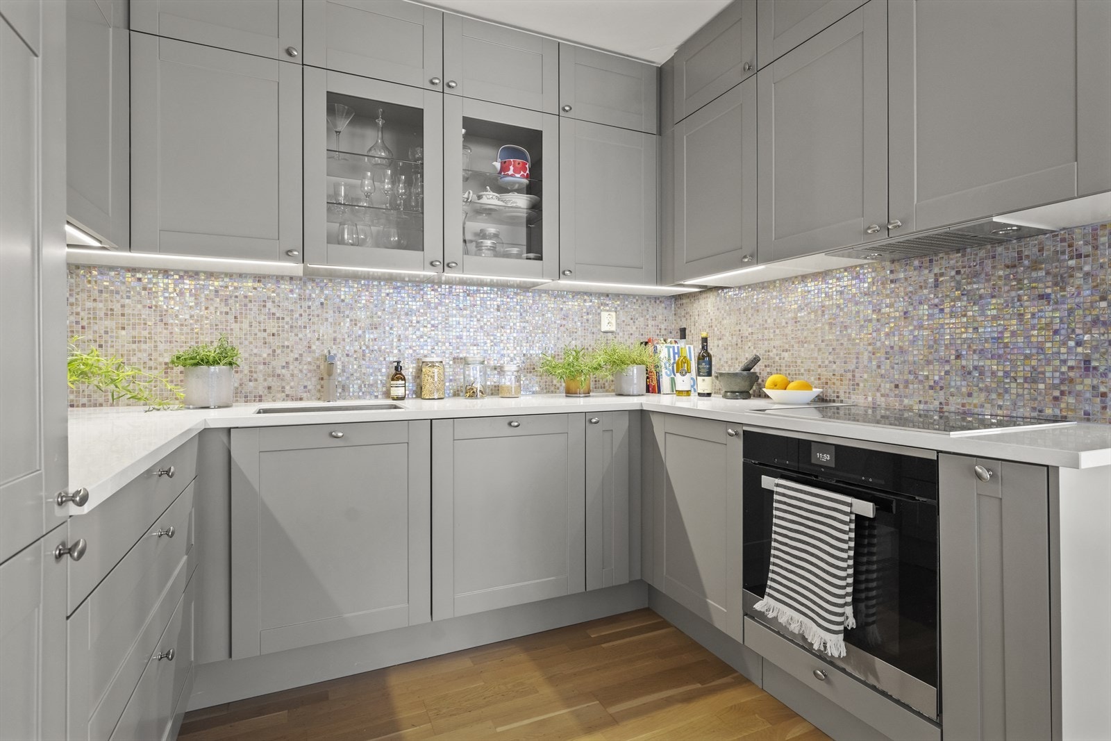 Meget pen HTH kjøkkeninnredning fra 2017 med profilerte grå fronter på skuffer og skap. Benkeplater i lys kompositt. Nedfelt induksjonstopp. Integrert oppvaskmaskin, kombinert kjøl/frys og stekeovn. Alle hvitevarer fra Míele Galleribilde