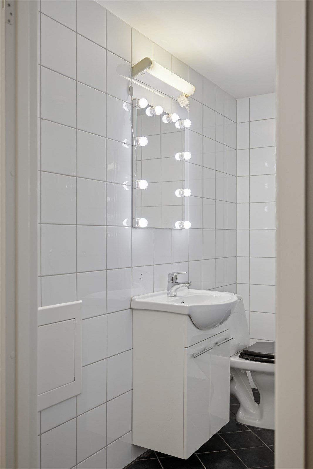 Badet er fra byggeåret og har flislagte overflater på både vegger og gulv. Det er speil og belysning over servanten. Galleribilde