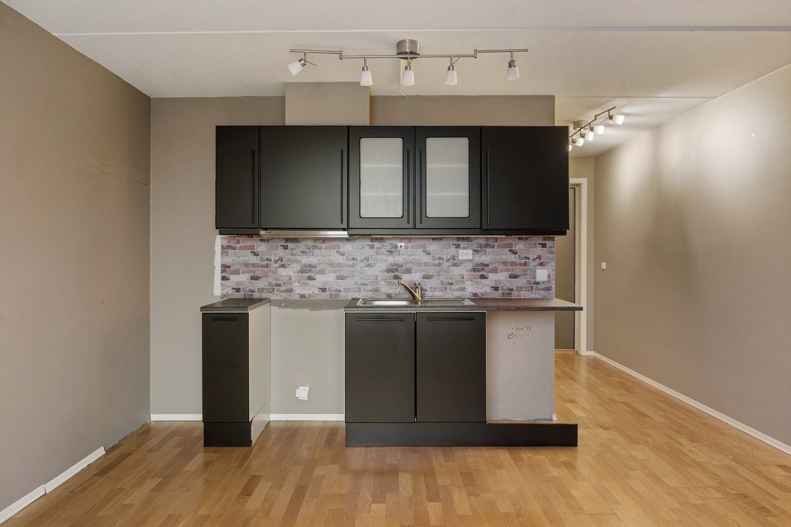 Kjøkkenet er fra byggeåret og har en mørktonet innredning med glatte, folierte fronter og benkeplate i laminat, utstyrt med en planlimt kum i rustfritt stål. Galleribilde