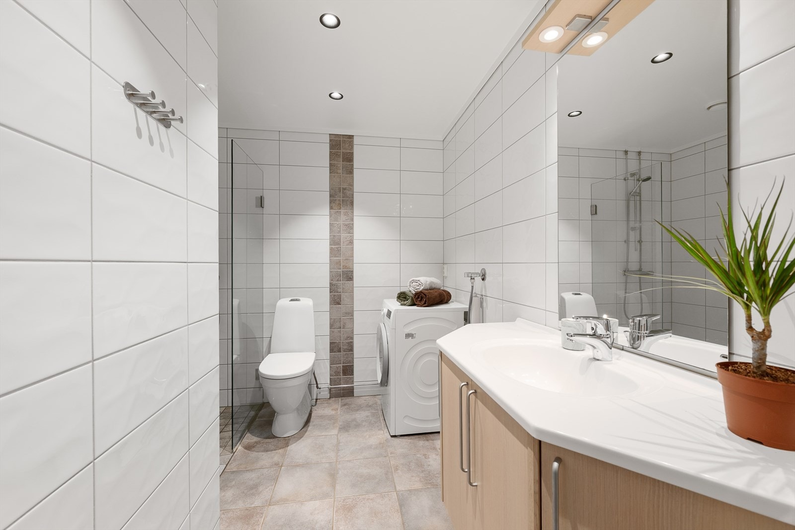 Lyst og flislagt baderom med opplegg for vaskemaskin. Galleribilde