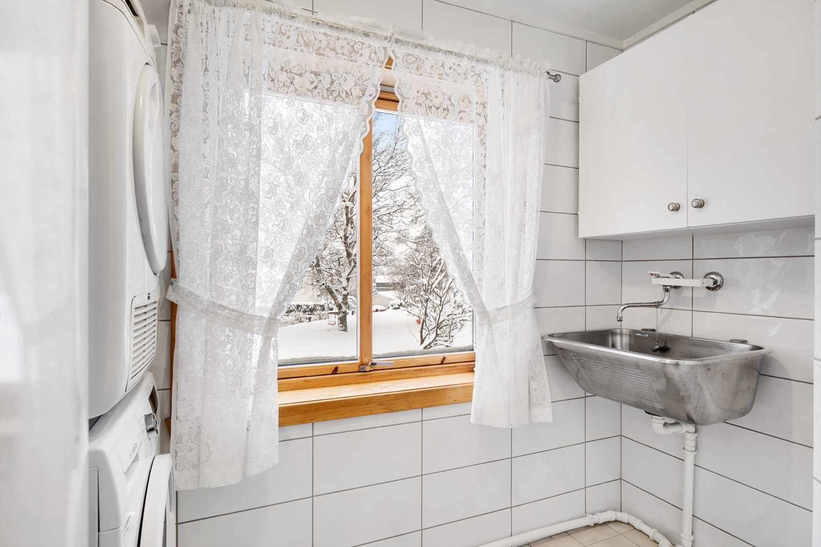 Vaskerom med fliser på vegger og gulv, innredet med servant og opplegg for vaskemaskin. Galleribilde