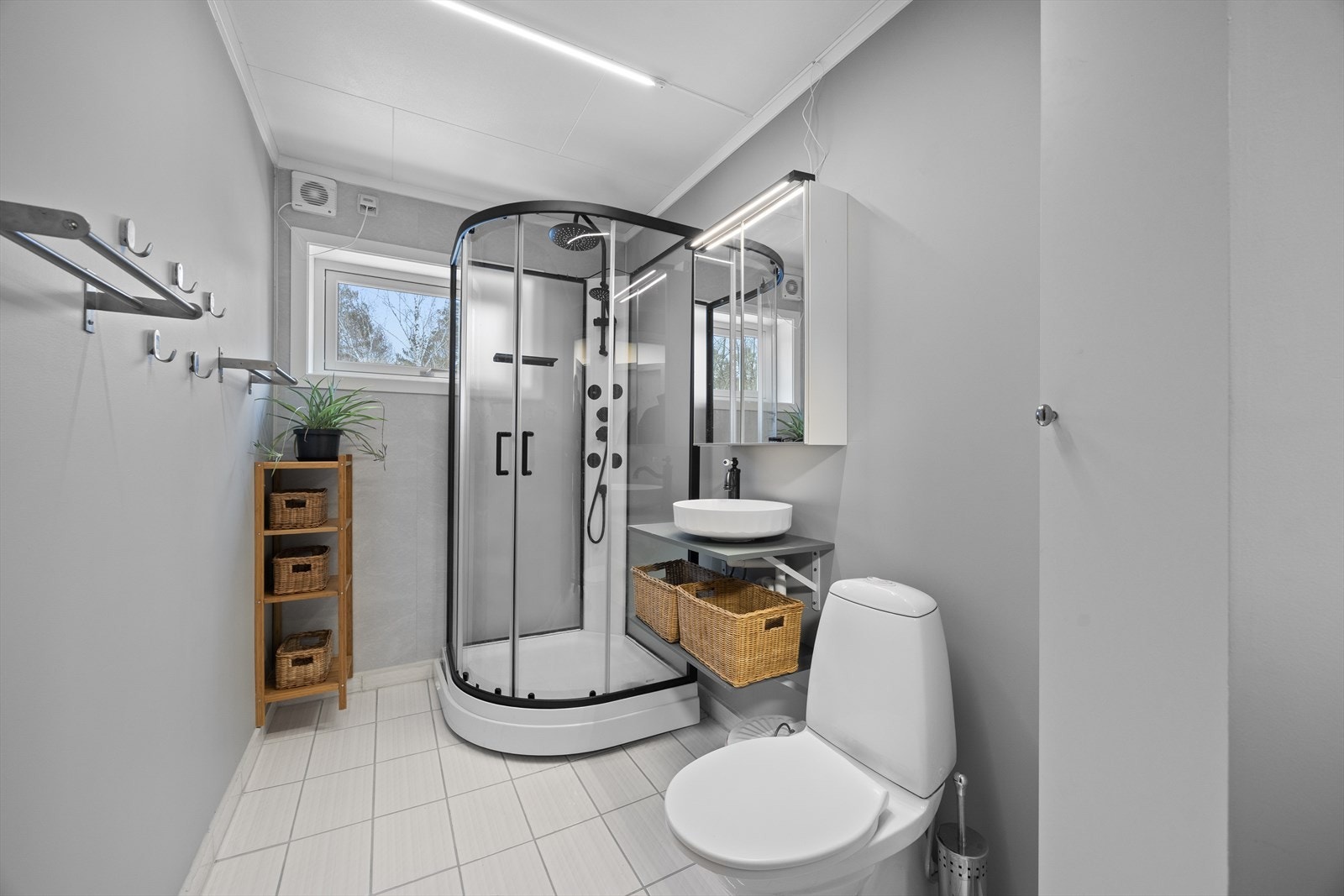 Badet har flislagt gulv og vegger med malte plater, samt dusjkabinett og servant. Galleribilde