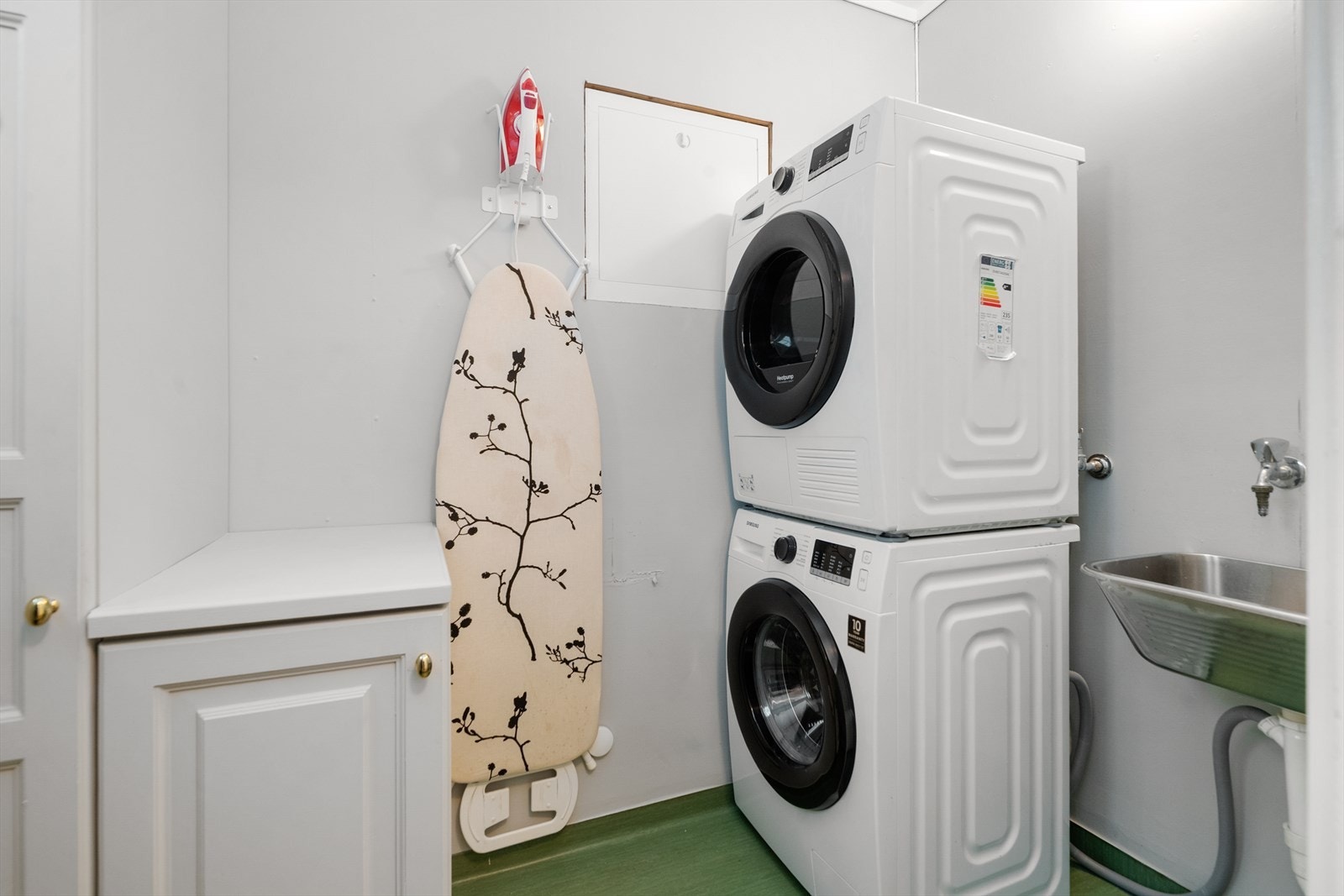 Eldre vaskerom med belegg på gulv og våtromstapet på vegger. Her er det utslagsvask og opplegg for vaskemaskin, samt praktisk oppbevaring. Galleribilde