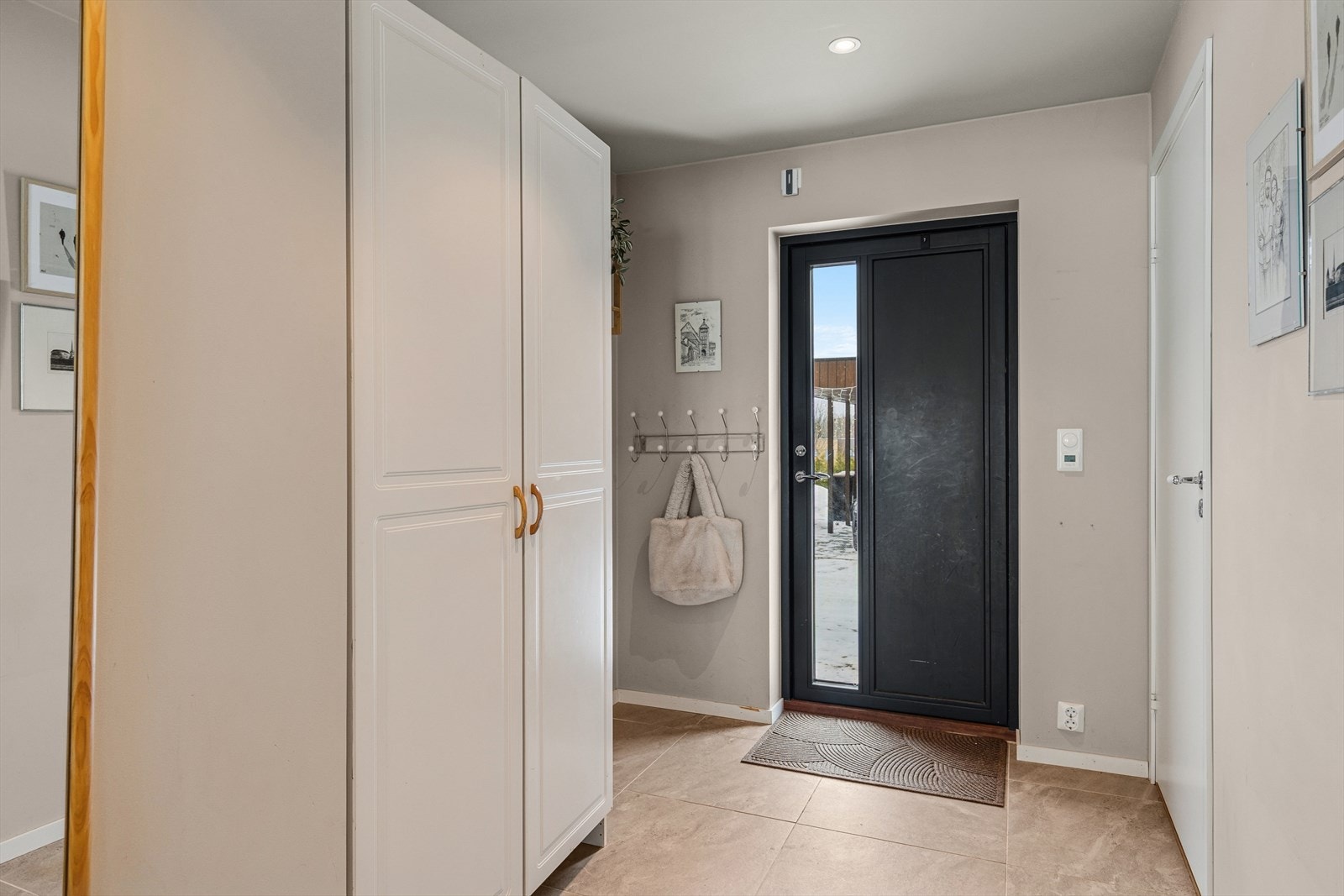 Boligen har en stilren sort ytterdør med glassfelt som slipper inn et behagelig og naturlig lys, og skaper en lys og innbydende atmosfære i entréen Galleribilde