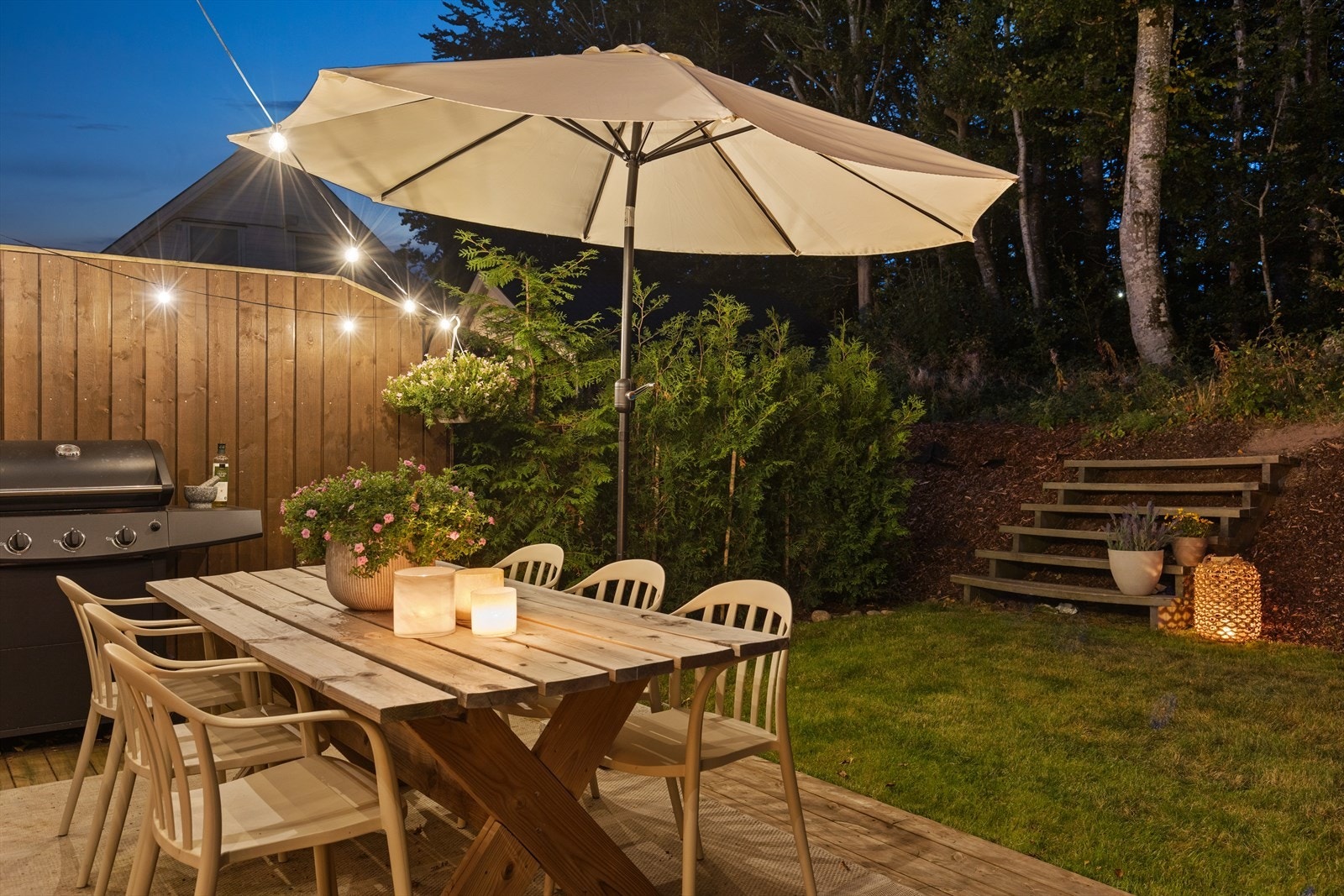 Hage med plen og terrasseplatting, platting med terrassebord og levegg med stående kledning - et perfekt sted for store utemøbler og lange sommerdager med sol i naturskjønne og rolige omgivelser Galleribilde