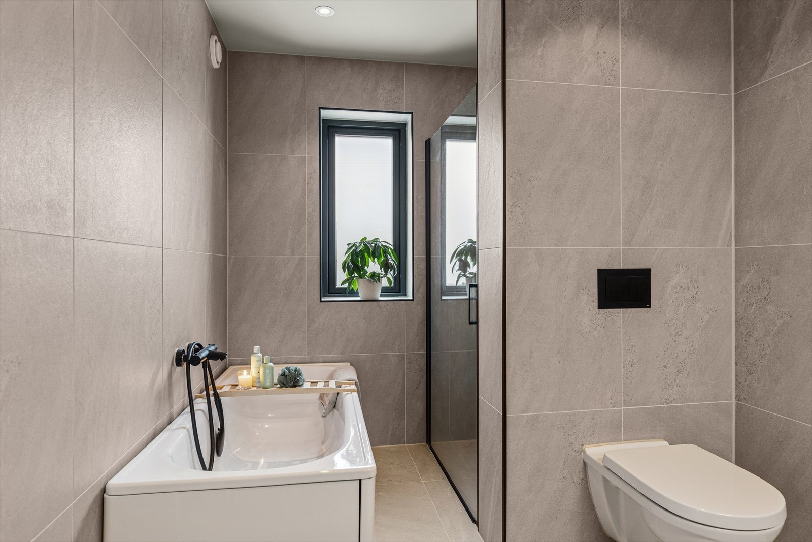 Badet er utstyrt med vegghengt toalett og en romslig dusjnisje adskilt med vegg og glassdør, samt badekar Galleribilde