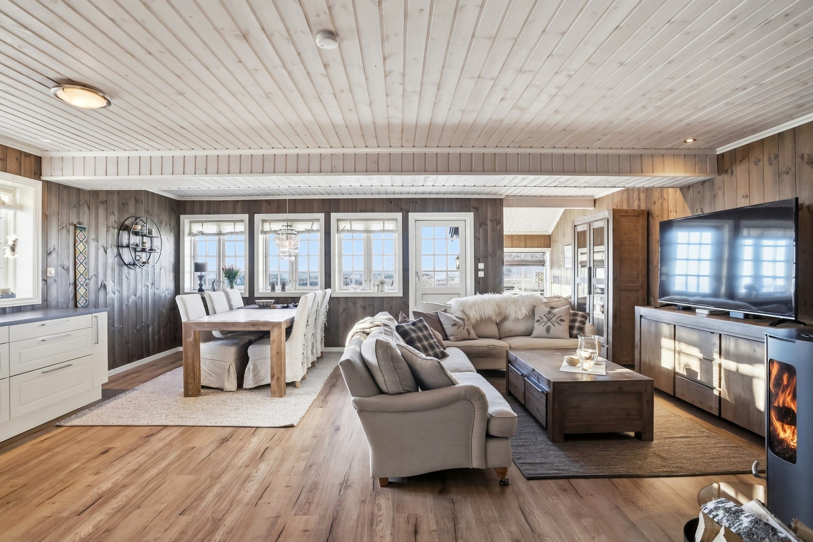 Stue og kjøkken i åpen løsning. Flere vindusflater slipper dagslyset inn Galleribilde