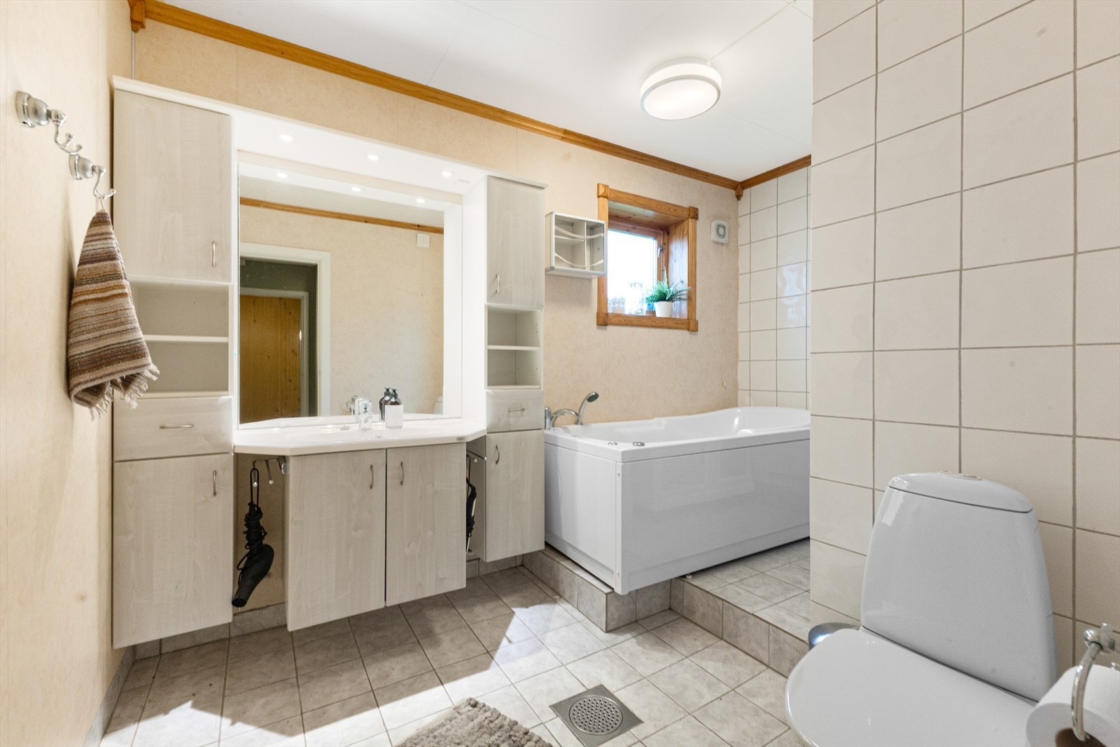 Badet har fliser på gulv med elektriske varmekabler, fliser og tapet på vegger og malte plater i tak. Galleribilde