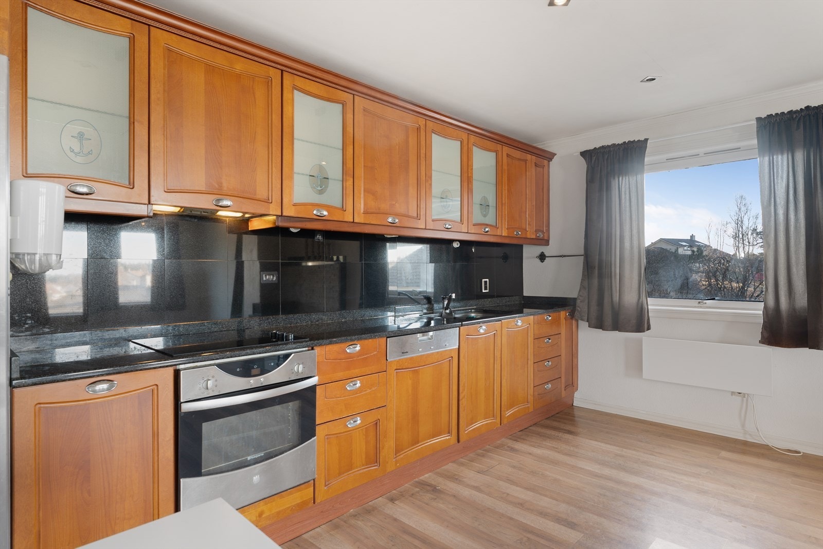 Flott kjøkken med gode kvaliteter med trestruktur og benkeplate i stein Galleribilde