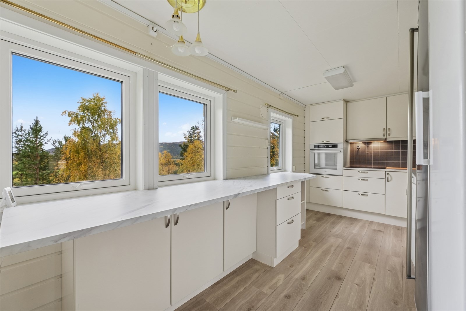 Arbeidsbenken er plassert ved vinduene, som slipper inn rikelig med dagslys og gir en flott utsikt mot naturen utenfor. Dette gir kjøkkenet en lys og trivelig atmosfære, og gjør det til et naturlig samlingspunkt i hjemmet. Galleribilde