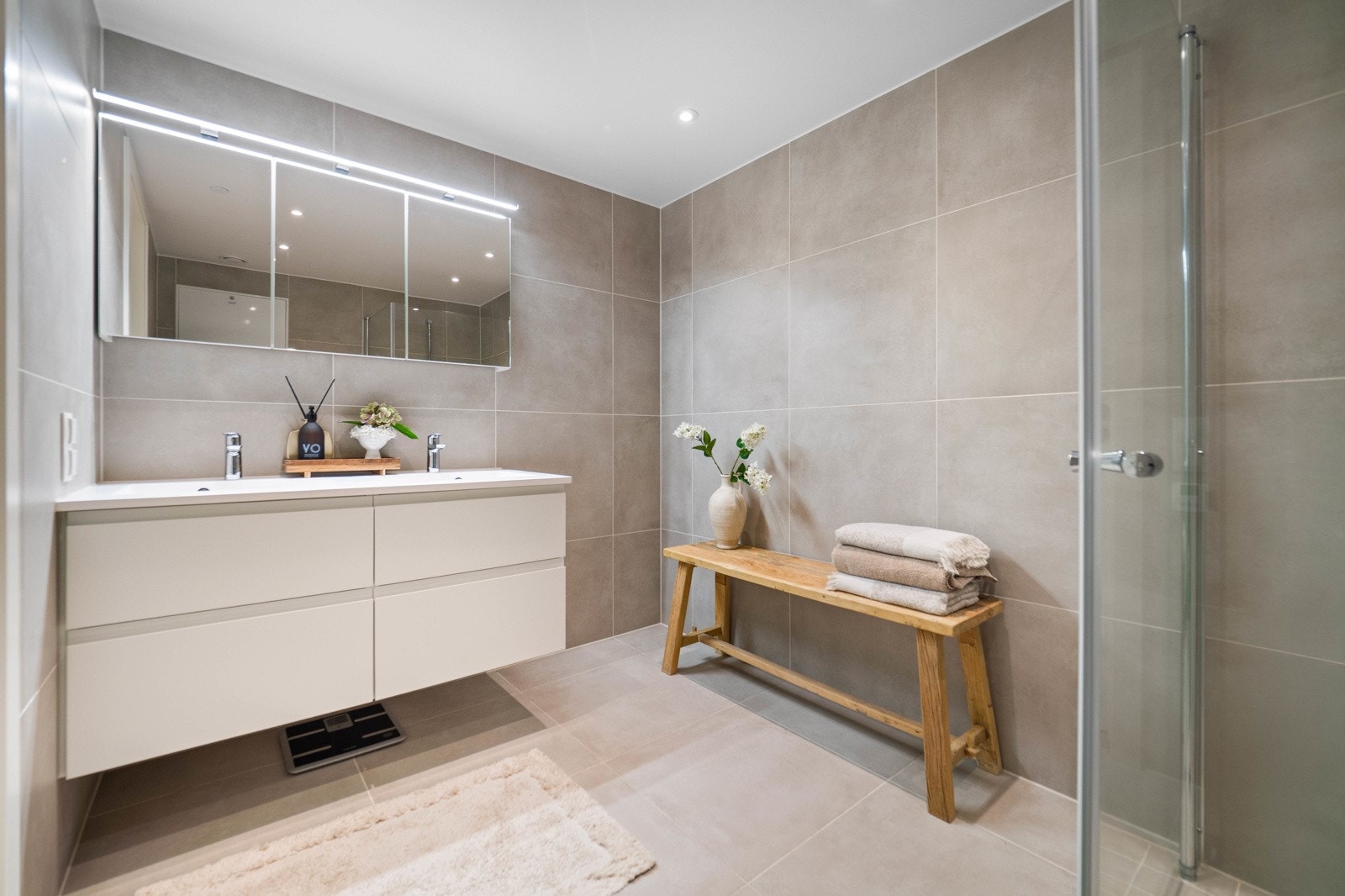 Begge bad er flislagt med varme i gulv. Vegghengt servantinnredning med skuffer og ovenpåliggende servant. Speilskap med lys, dusjhjørne med dører og vegghengt toalett. Galleribilde