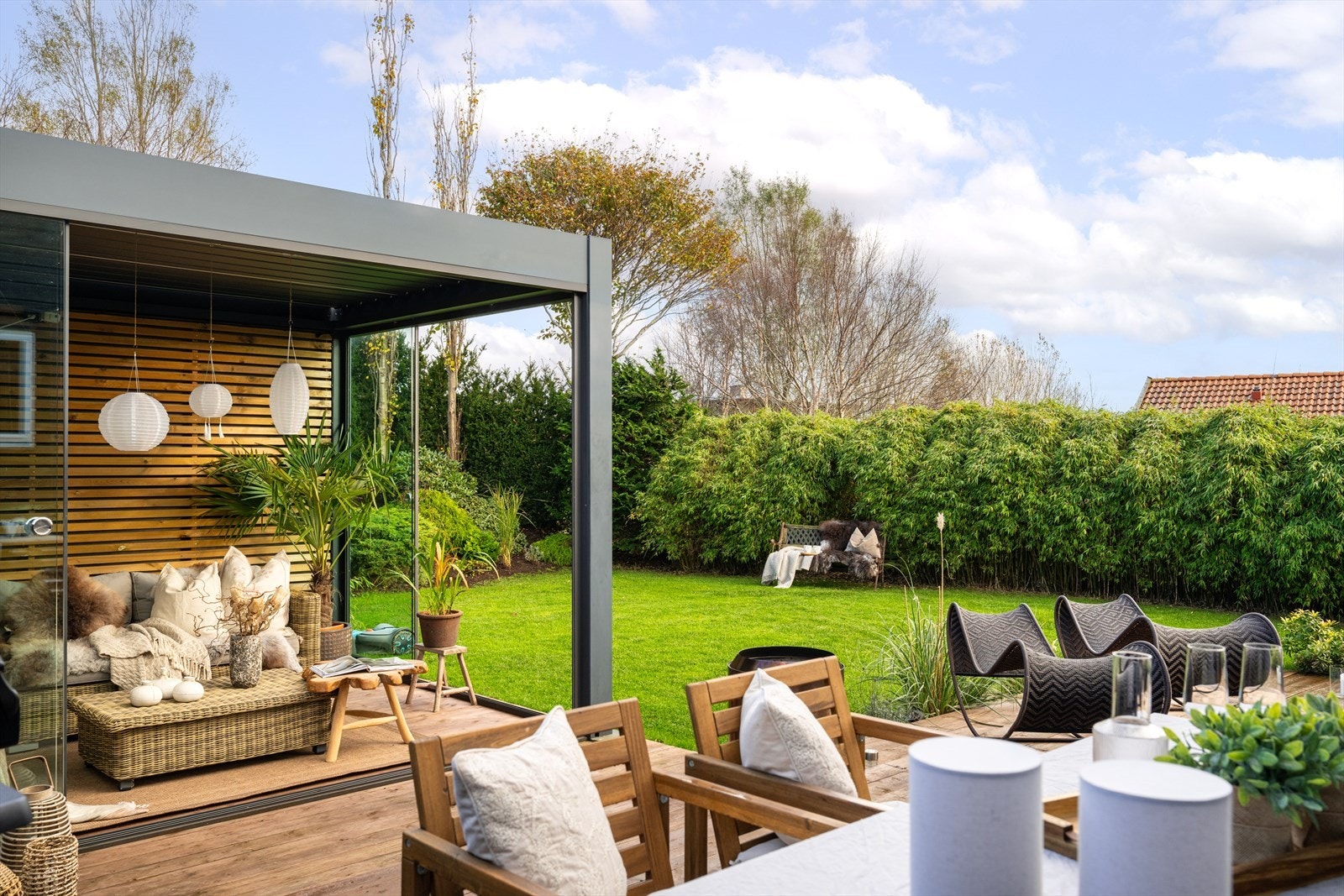 Gjennomført uteplass med terrasse i tre, pergola og frodig beplantning som gir en lun og privat atmosfære. Galleribilde