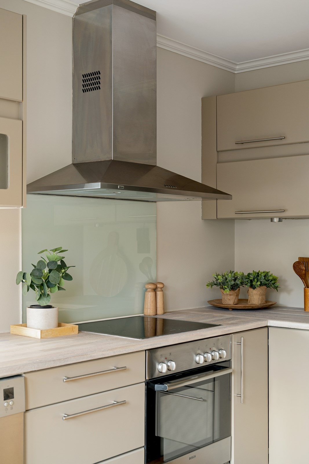 Delikat kjøkken med integrerte hvitevarer, glassplate over benk og stilren ventilator i børstet stål. Galleribilde