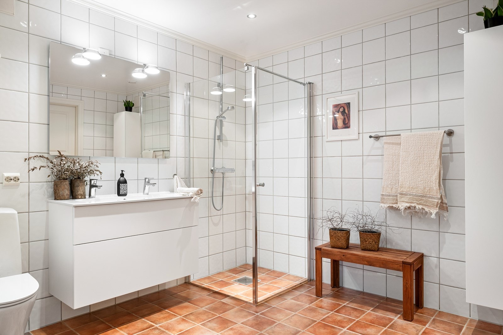 Romslig, flislagt bad med varmekabler i gulv, dusjhjørne med glassvegger, servant med underskap og speil. Galleribilde