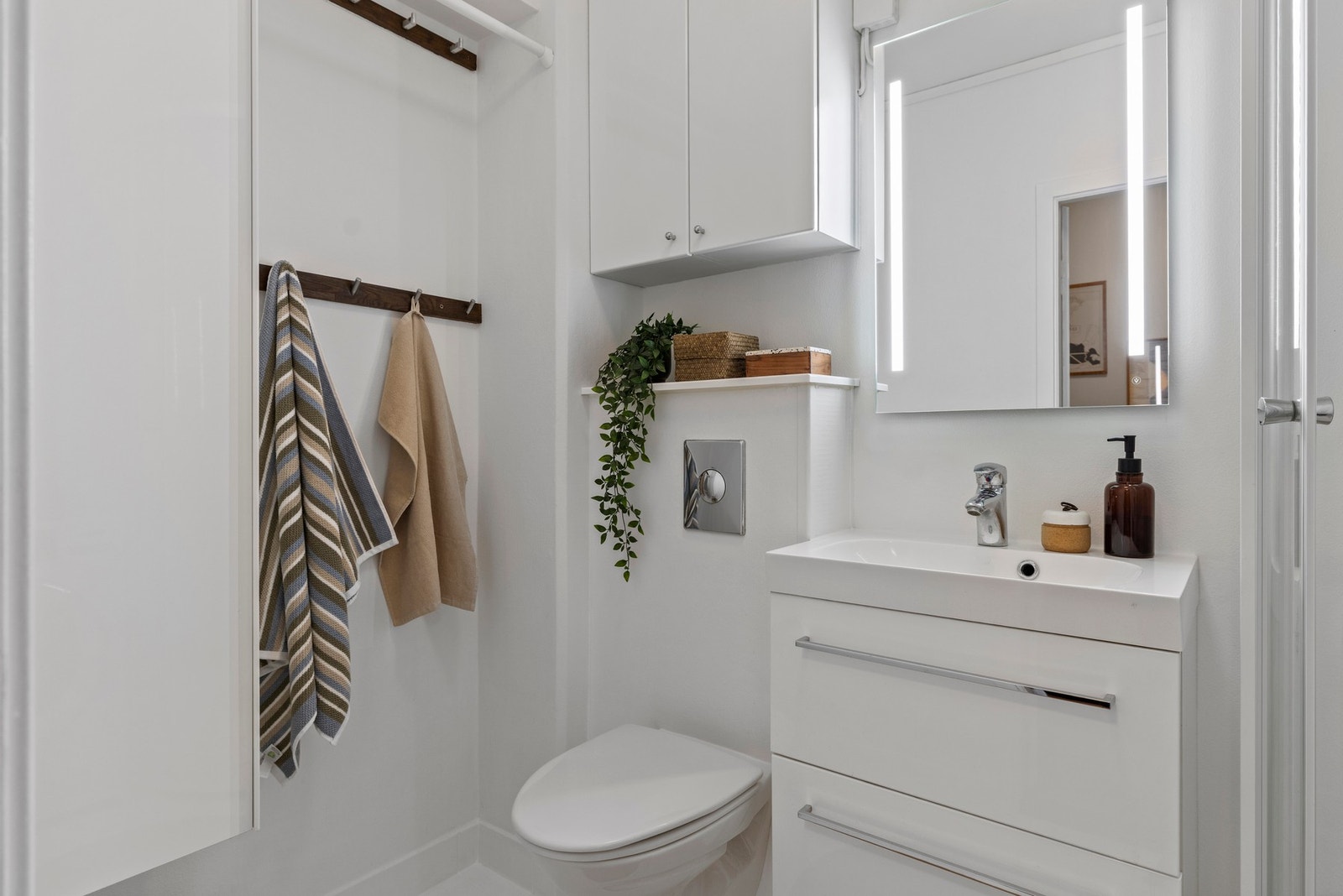 Veggmontert servantskap med heldekkende vask og ett-greps armatur i krom. Innebygget sisterne med vegghengt toalett. Galleribilde