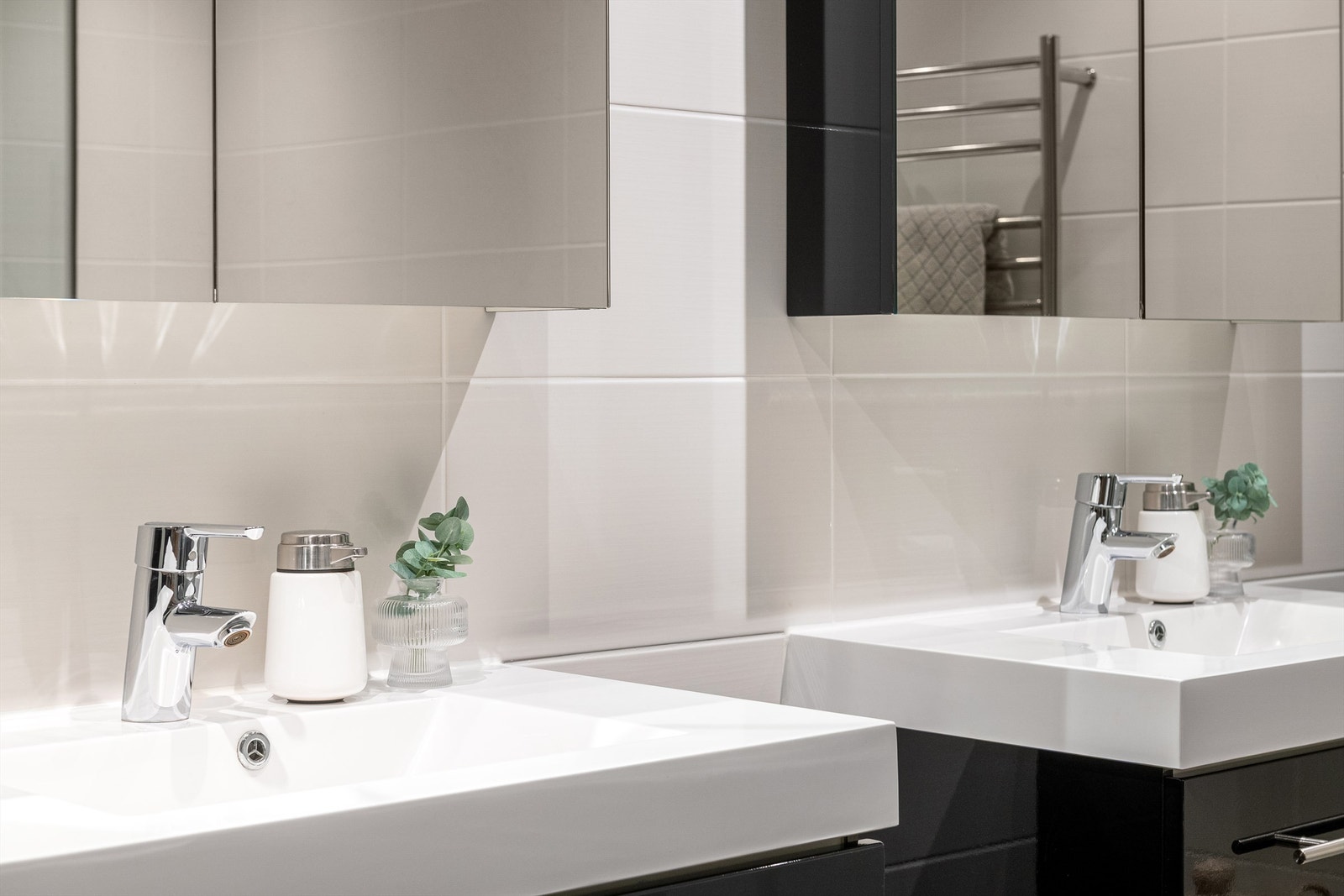 To servantskap med malte fronter og heldekkende servanter. Overskap med speil og lys på veggen over servantene. Galleribilde