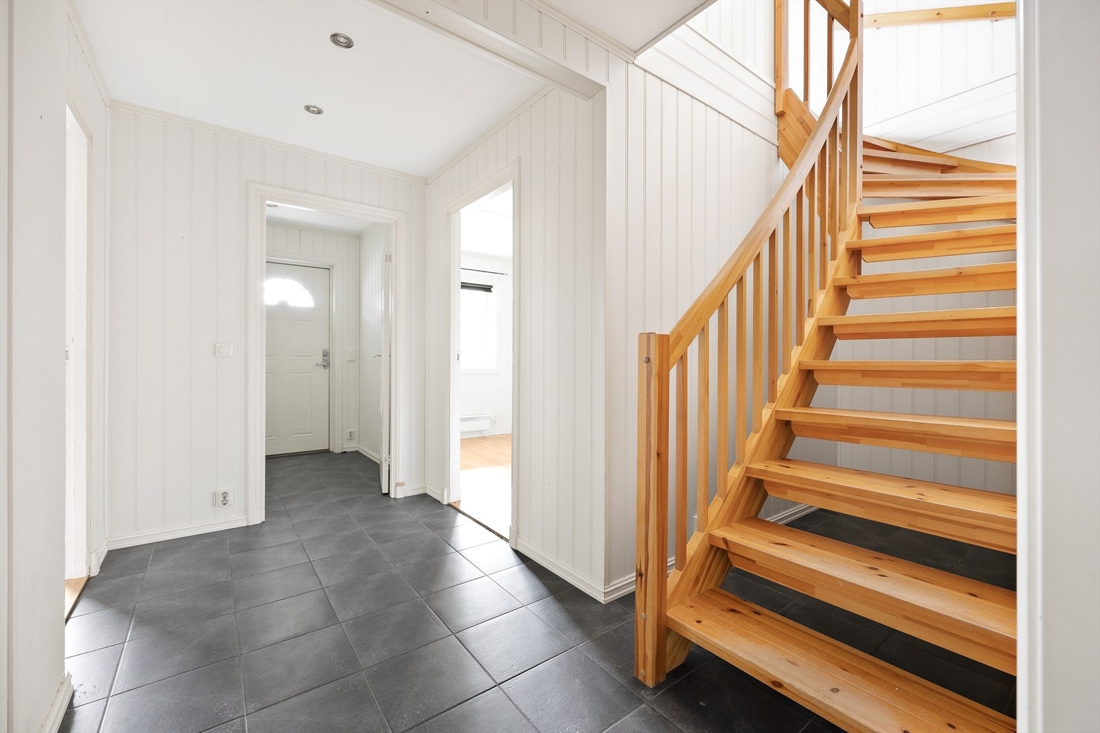 Du kommer inn i en hall med flislagt gulv. Den lakkerte tretrappen leder opp til hovedetasjen. Galleribilde