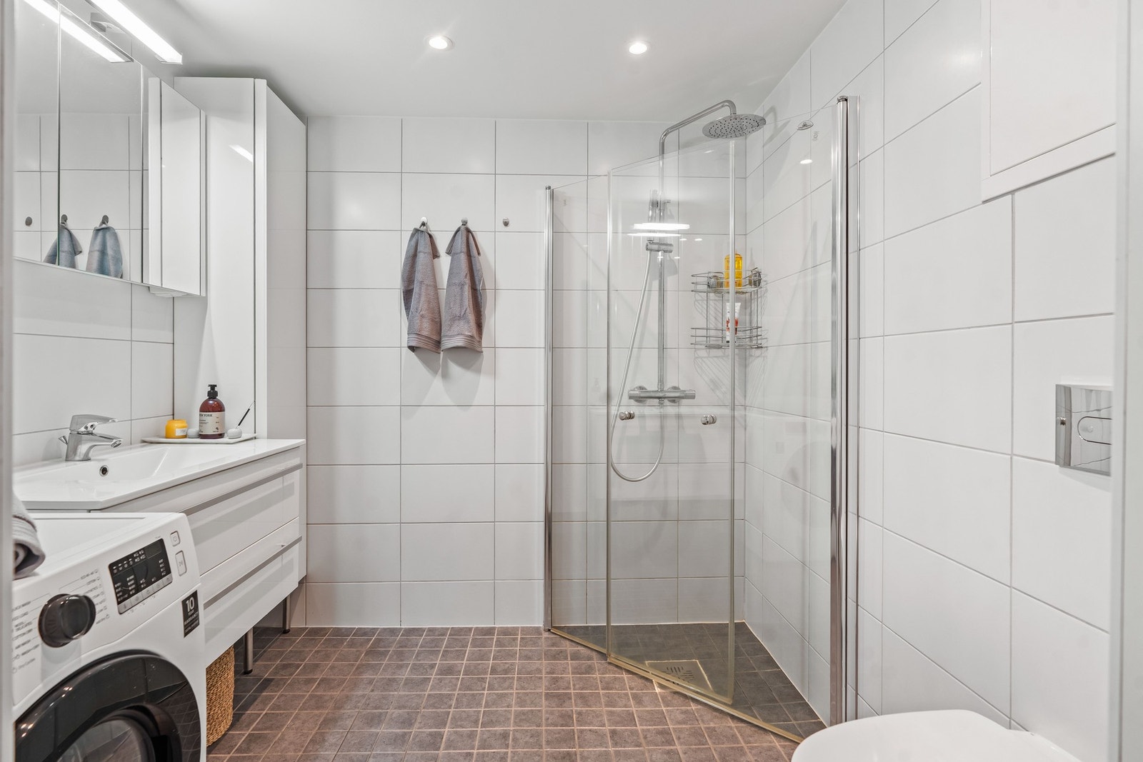 Badet inneholder servant med under-, over- og sideskap, speil med belysning og stikkontakt. Dusjløsning med dusjing direkte på gulv og vegg. Galleribilde