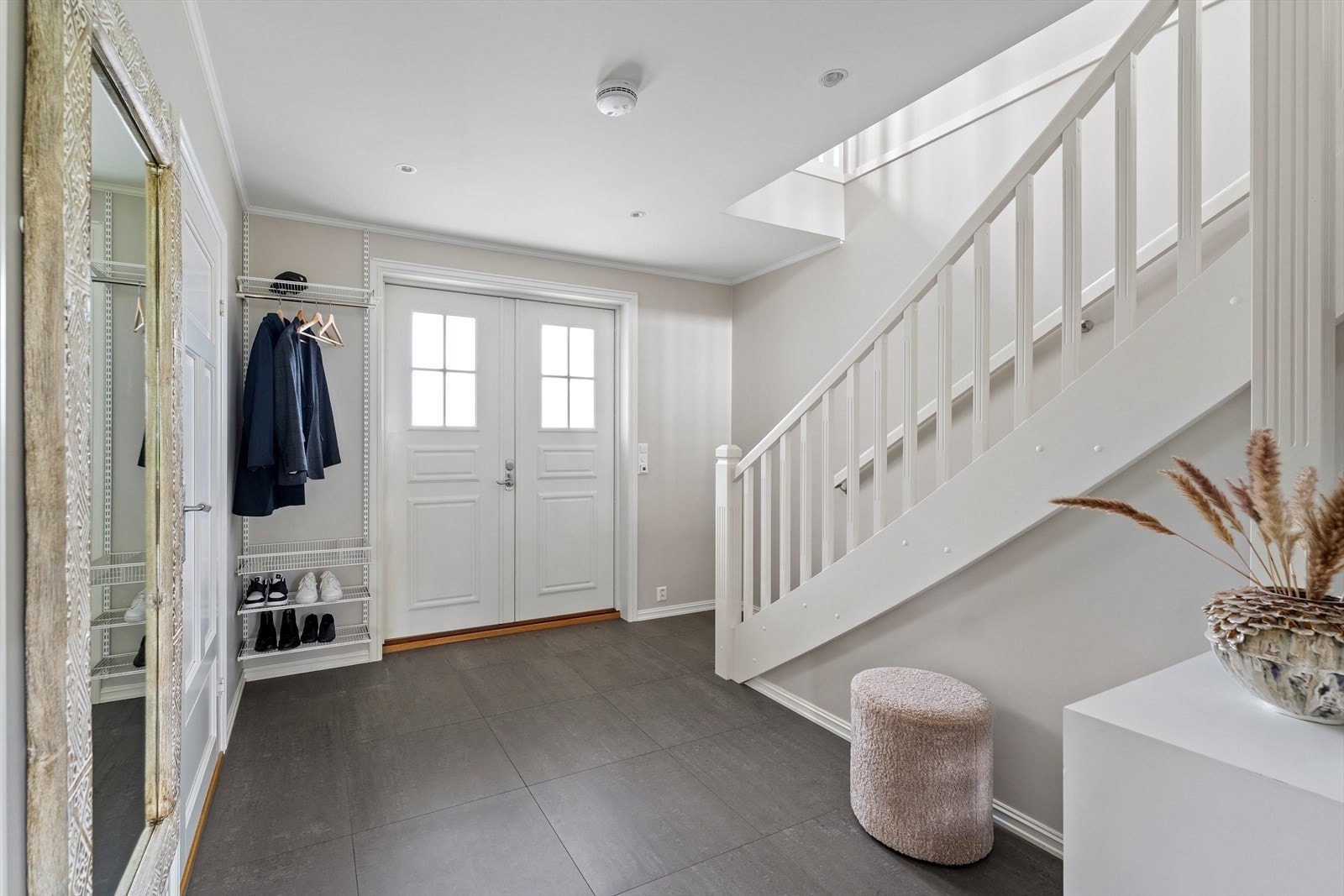 Boligen har inngang til en innbydende hall, samt bi-inngang til vaskerommet, noe som er praktisk med småbarn og firbente i hus. Gulvvarme i hele første etasje og grå fliser på gulvet i hallen. Galleribilde