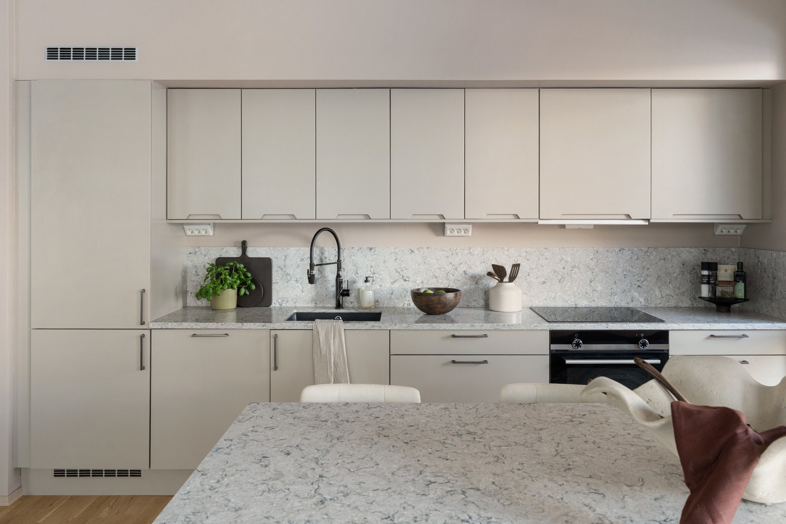 Stilrent kjøkken fra HTH med beige over og underskap, kombinert med en elegant benkeplate som også er ført opp langs veggen som backsplash. Galleribilde