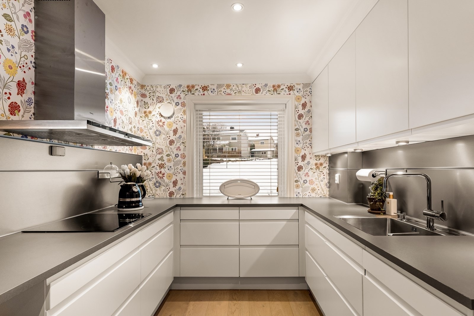 Kjøkkenet har en spennende tapet som tilfører rommet karakter, kombinert med downlights i himlingen som gir en moderne og behagelig belysning. Flotte stålplater over benkene sørger for både et elegant uttrykk og enkel rengjøring. Galleribilde