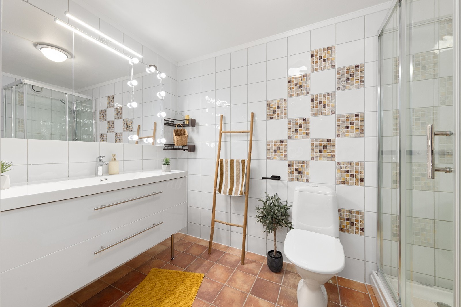 Badet er flislagt og har elektrisk gulvvarme for økt komfort. Rommet er utstyrt med en innredning som inkluderer en nedfelt servant og et dusjkabinett. Galleribilde