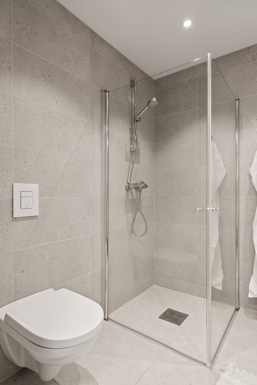 Delikat, flislagt bad med vegghengt toalett og dusjhjørne med glassdører. Galleribilde