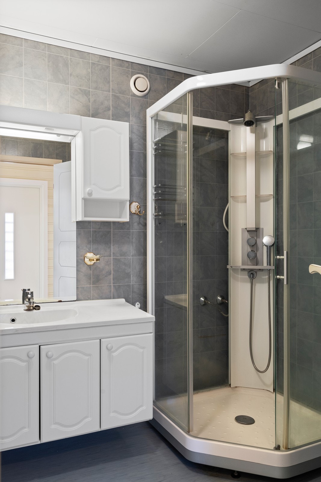 Badet er innredet med servant på skap, frittstående toalett og dusjkabinett. Galleribilde