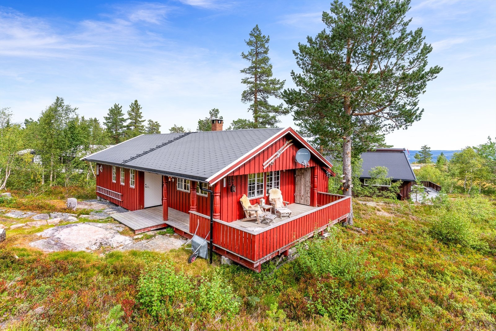 Sommerbilde av hytta. Adkomstpartiet er hyggelig og skjermet, med en solrik uteplass og mulighet for benkegruppe rundt ei hyggelig bålpanne. Galleribilde