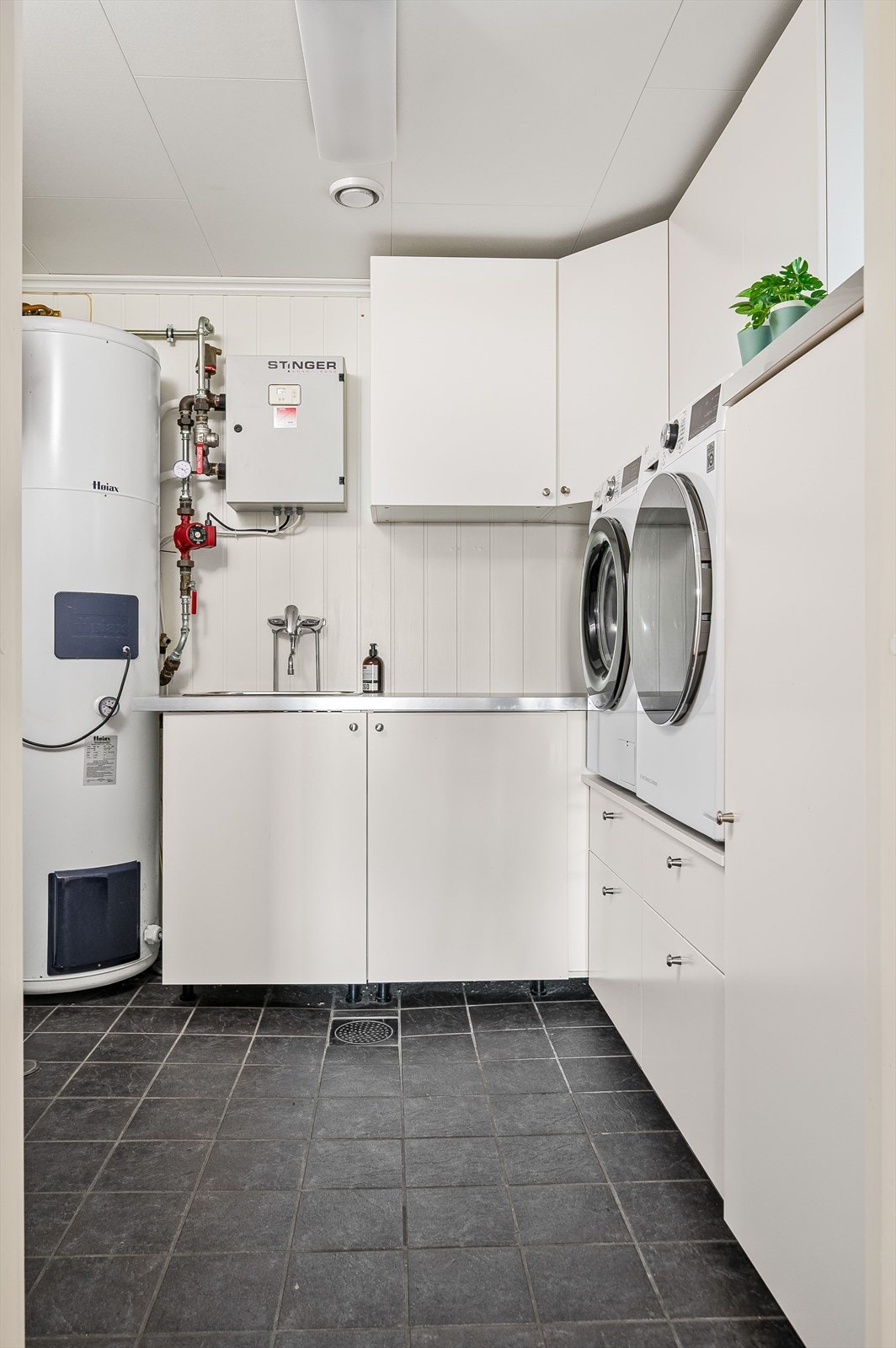 Separat vaskerom med flislagt gulv med sluk og mekanisk avtrekk. Lys innredning med masse skapplass og benkeplate med nedfelt utslagskum. Praktisk med plass og opplegg for både vaskemaskin og tørketrommel i behagelig arbeidshøyde. Galleribilde