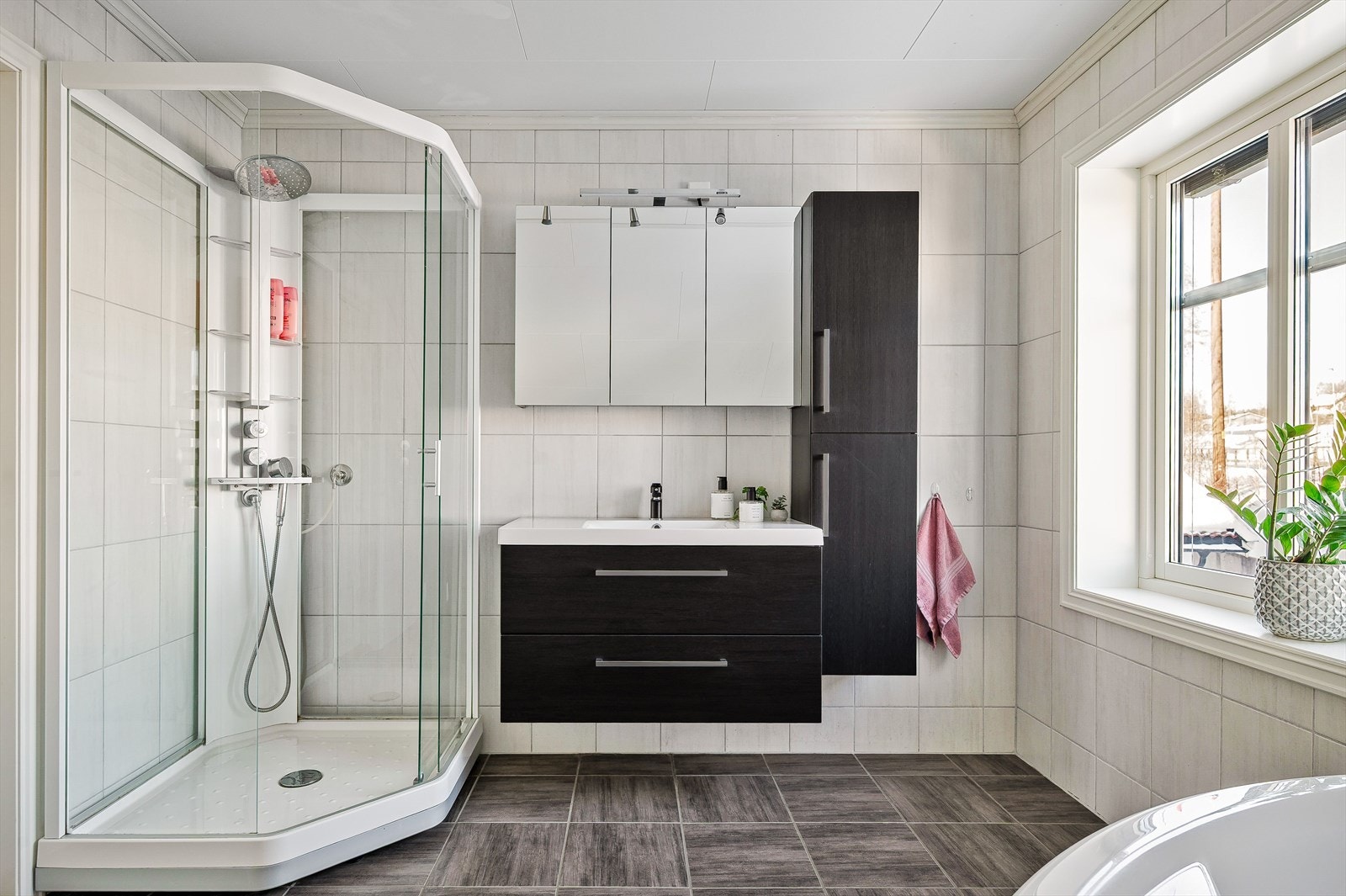 Moderne baderomsinnredning med skuffer og heldekkende servant, speilskap med belysning over. Baderommet er også utstyrt med vegghengt høyskap, dusjkabinett med regnfallsdusj, badekar og toalett. Galleribilde