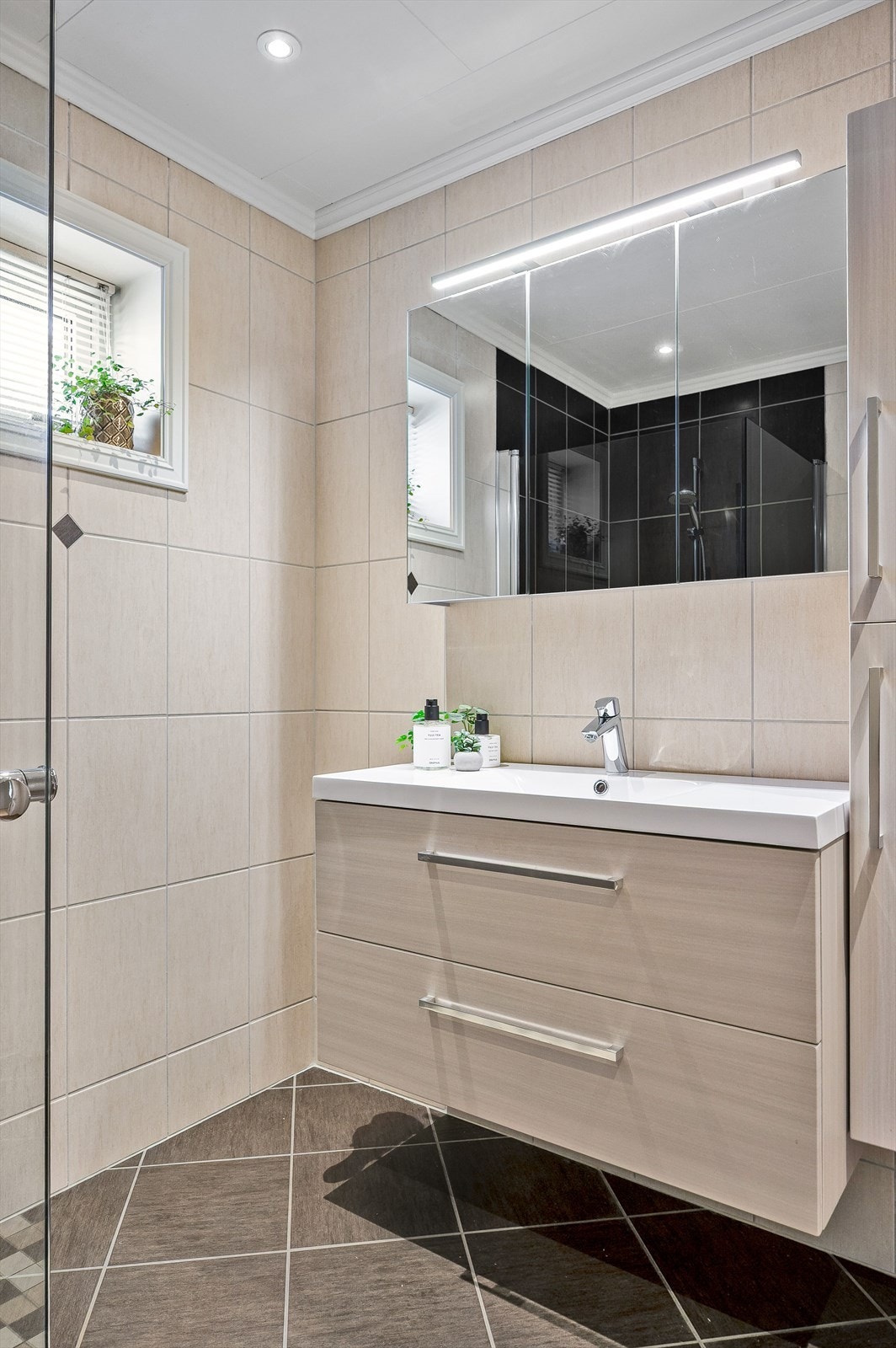 Moderne baderomsinnredning med skuffer og heldekkende servant, speilskap med belysning over. Baderommet er også utstyrt med ekstra høyskap, dusjhjørne med glassdører og toalett. Galleribilde