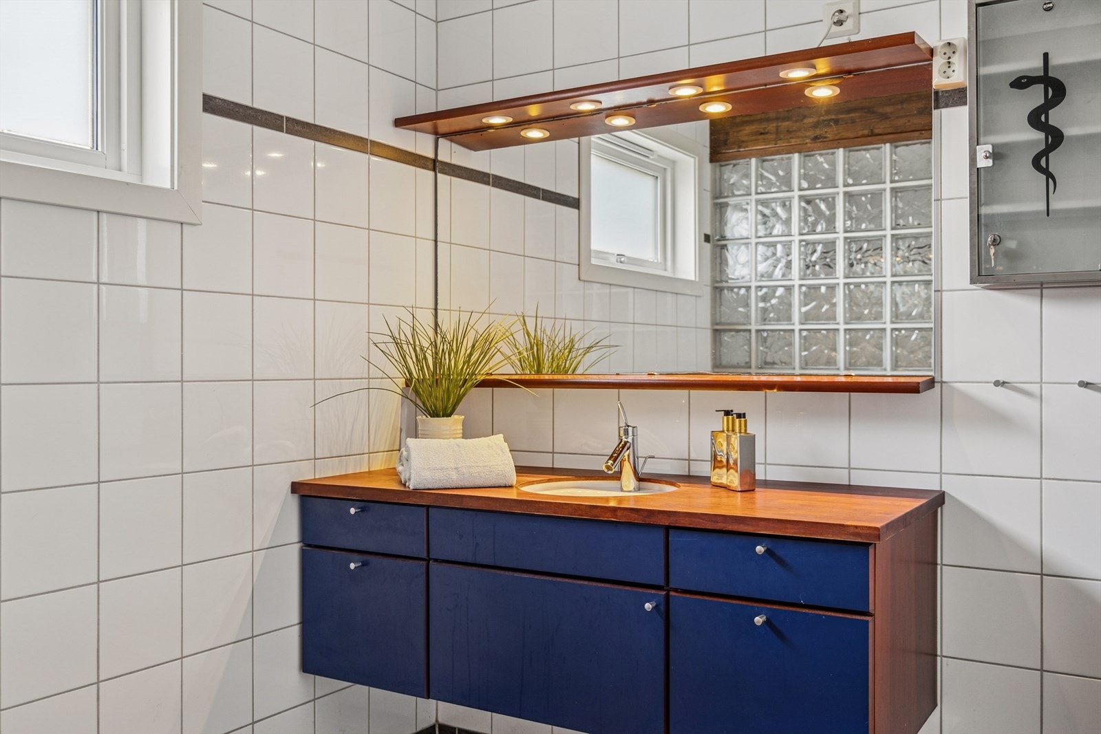 Flislagte vegger gir et moderne uttrykk på badet, som er utstyrt med servant og speilbelysning. Galleribilde