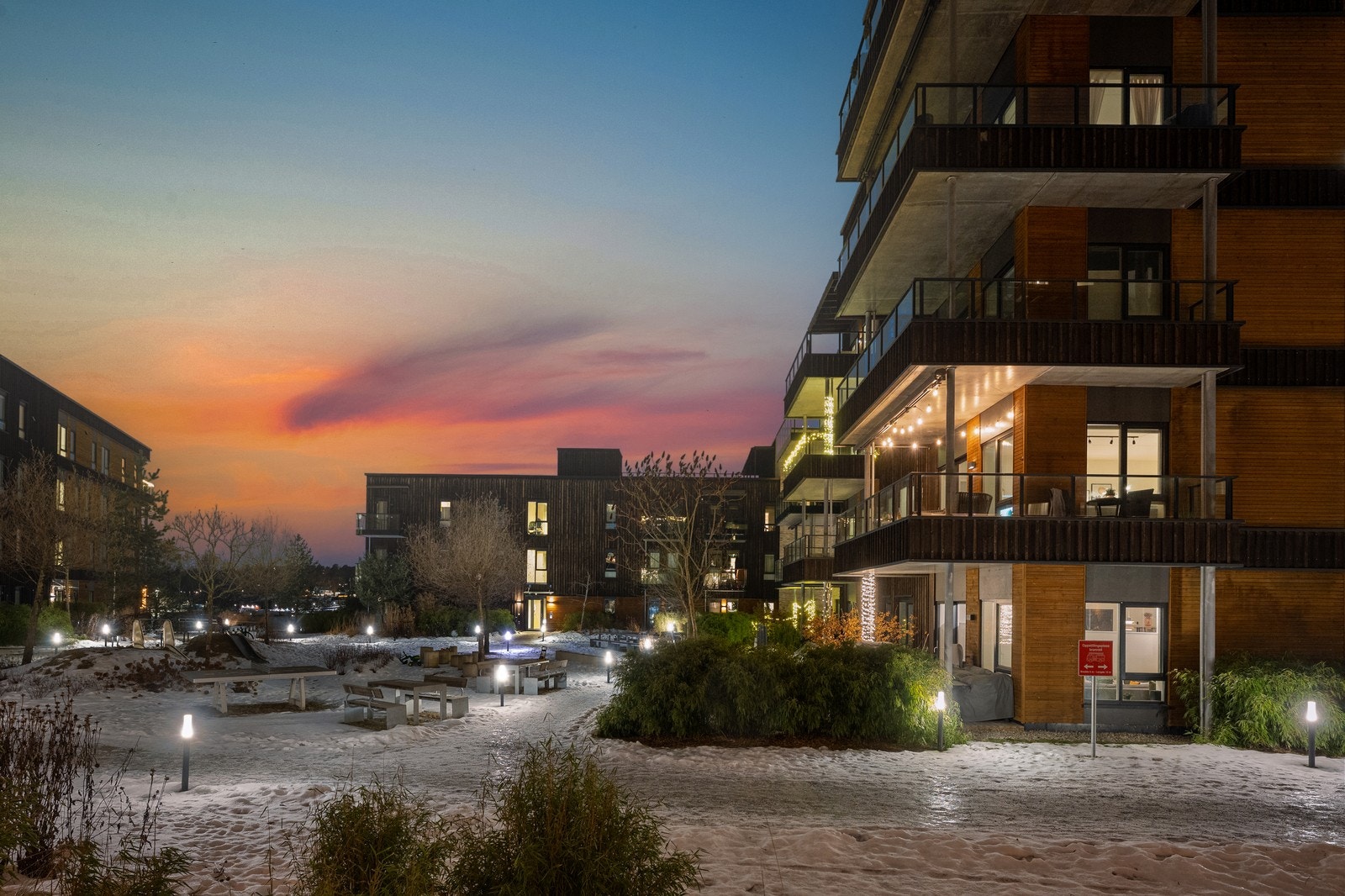 Moderne leilighetsbygg med balkonger gir utsikt over et opplyst og velholdt uteområde. Galleribilde