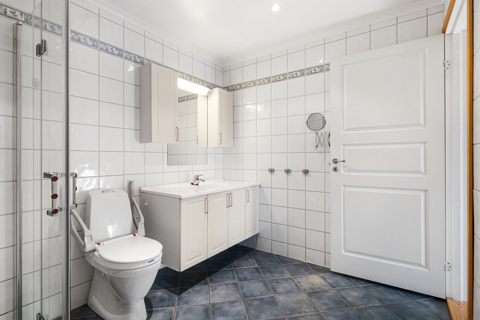 Et lyst og romslig bad som kombinerer funksjonalitet og stil! Fliser på både gulv og vegger skaper et elegant og tidløst uttrykk, mens det malte taket med moderne spotter gir en behagelig belysning. Galleribilde