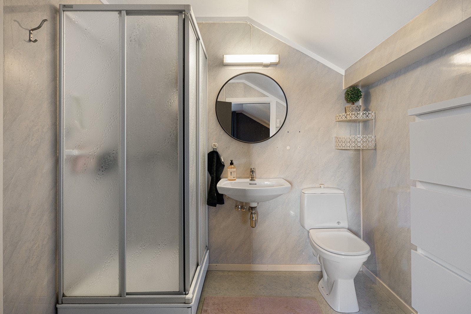 Badet i 2. etasje har lyse våtromsplater på veggene og grått belegg på gulv med sluk. I tillegg til et toalett har badet en vegghengt servant, speil, belysning og dusjkabinett. Galleribilde