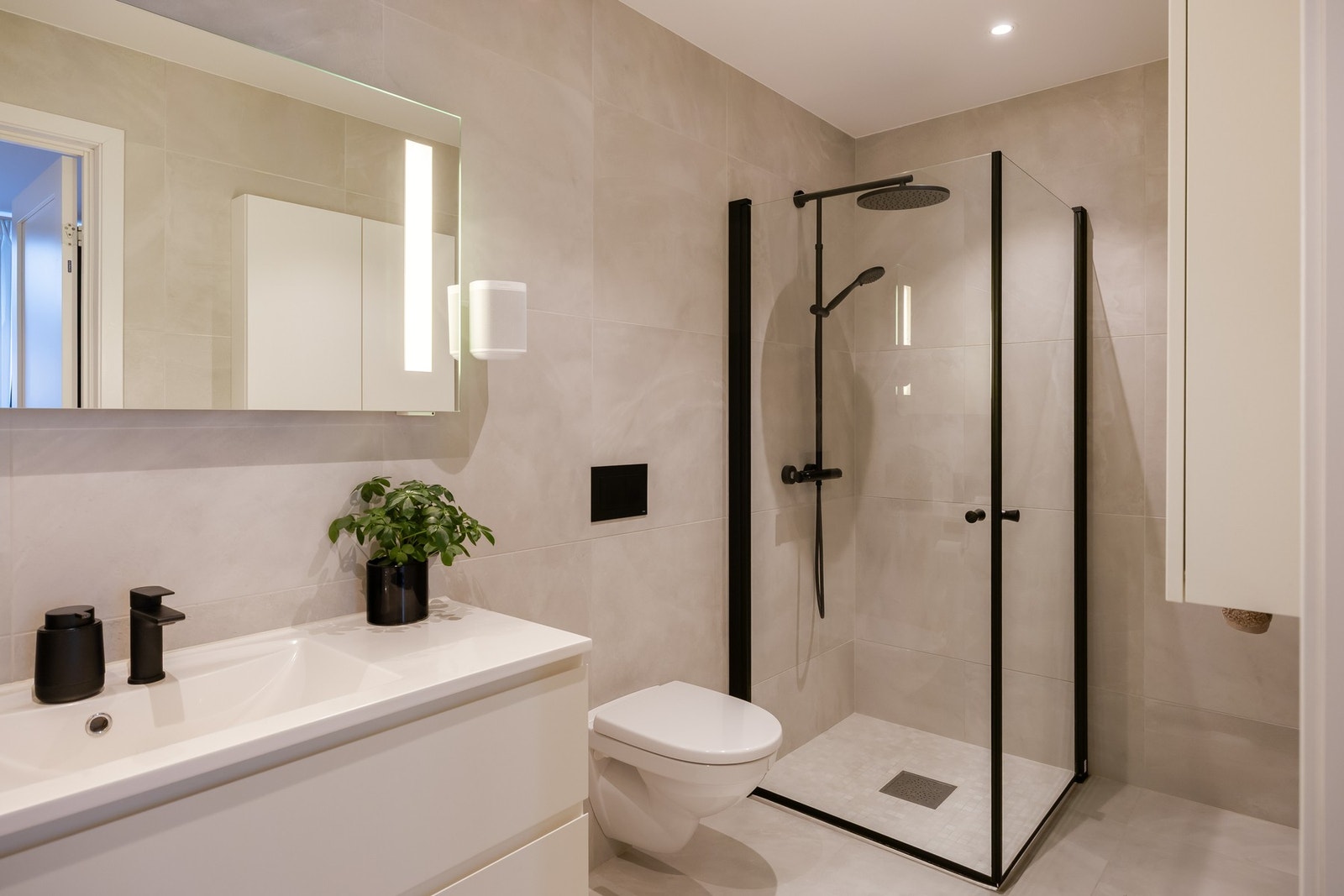 Badet ved hovedsoverom er pent med store 60 x 60 fliser på vegger og gulv. Badet er på 5m² og er utstyrt med baderomsinnredning, vegghengt toalett og dusjhjørne med innfellbare glassdører. Varmekabler i gulv. Galleribilde