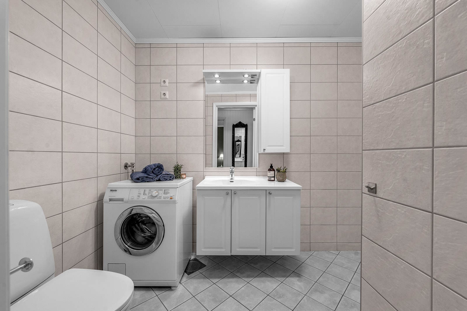 Helfliset baderom i 1. etasje. Vegghengt servantskap med heldekkende servant og ettgreps armatur. Speil over servant med overlys. Gulvmontert toalett. Opplegg for vaskemaskin. Galleribilde