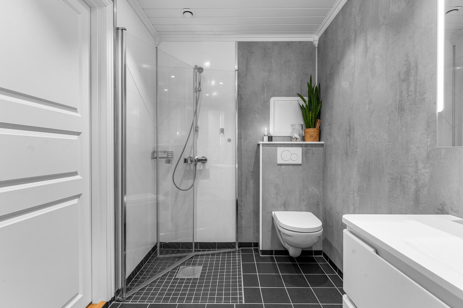 Baderom i 2. etasje fra 2019. Flislagt gulv med elektrisk gulvvarme. Veggflater kledd med våtromsplater. Malte panelplater med downlights i himling. Dusjnisje med innfellbare glassdører og dusjarmatur. Galleribilde